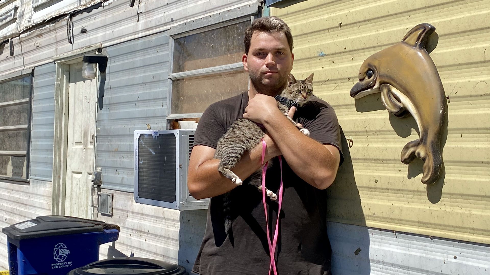 Anthony Lehman poses in front of his mobile home while holding his tabby cat Rocky.