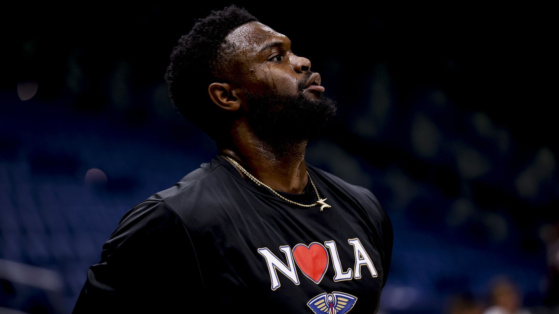 A photo of Zion Williamson as he looks up. He wears a NOLA T-shirt with a heart on the O and the Pelicans logo underneath.