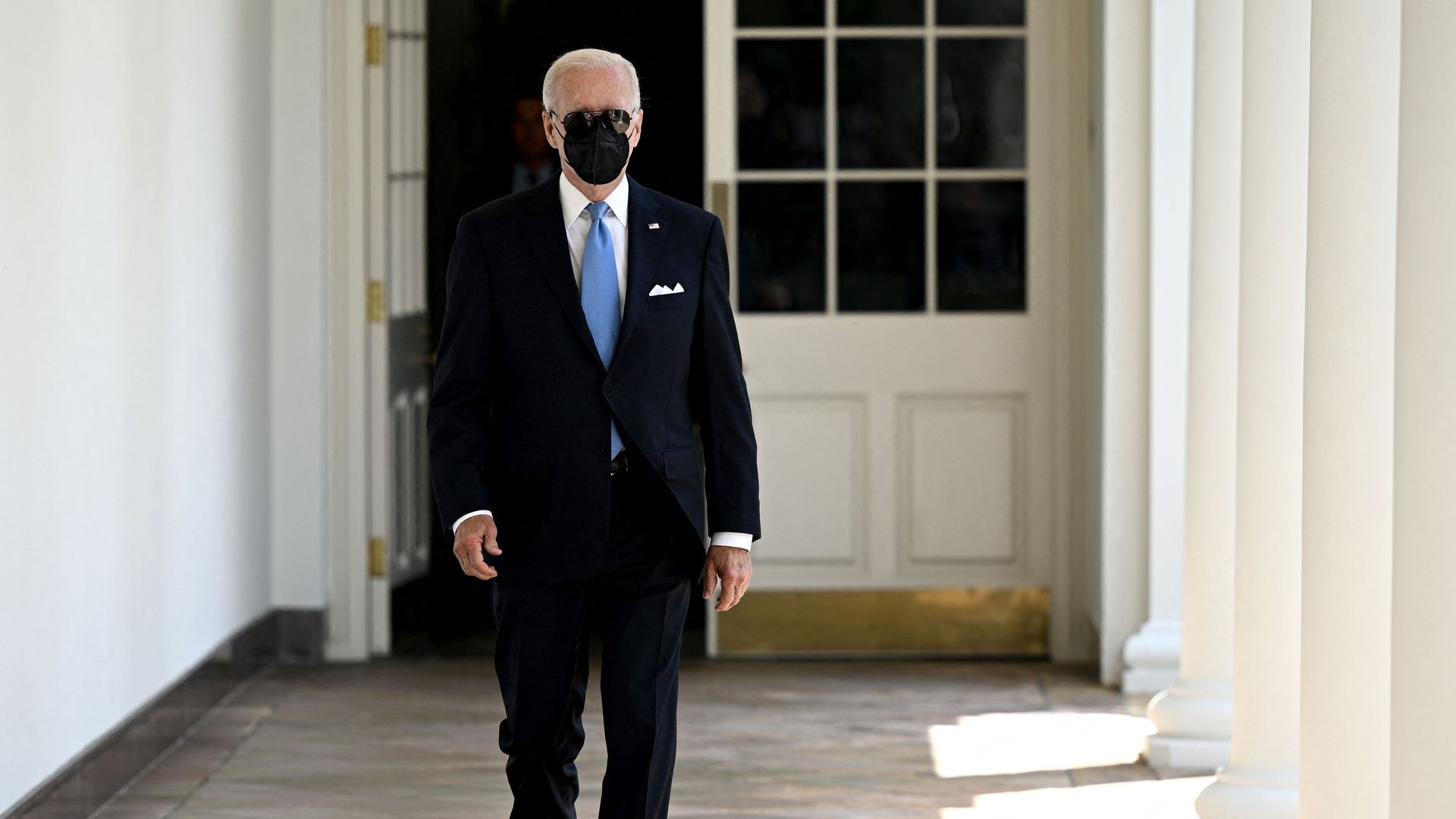 President Biden, wearing a mask, walks out of the White House toward the Rose Garden.