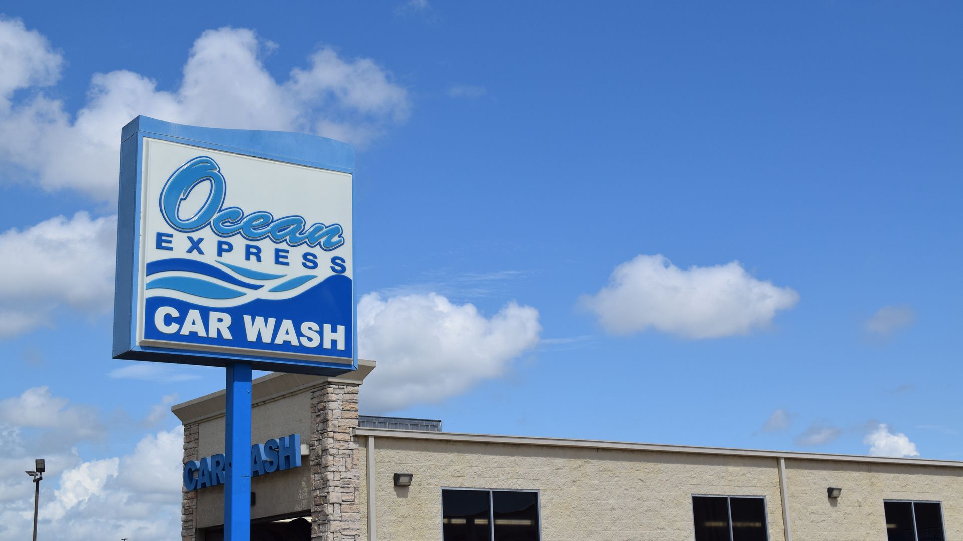 A blue and white sign reading "Ocean Express Car Wash" against a blue sky with a tan building in the background