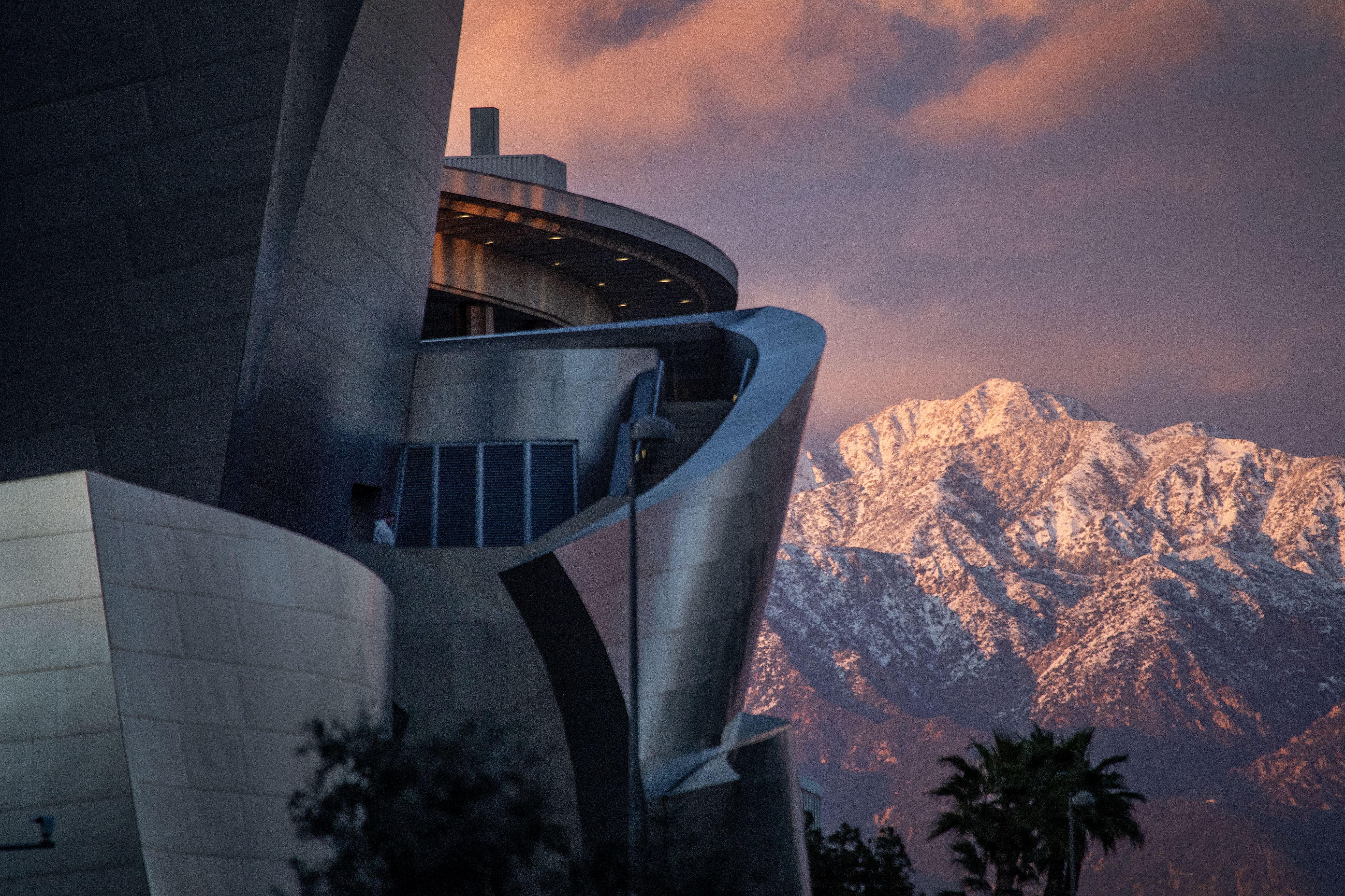 A person gets a high-angle view from the Walt Disney Concert Hall as it is viewed with the snow-capped San Gabriel mountains at sunset after historic rain and snow dumped on Southern California Wednesday, March 1, 2023 in Los Angeles. 