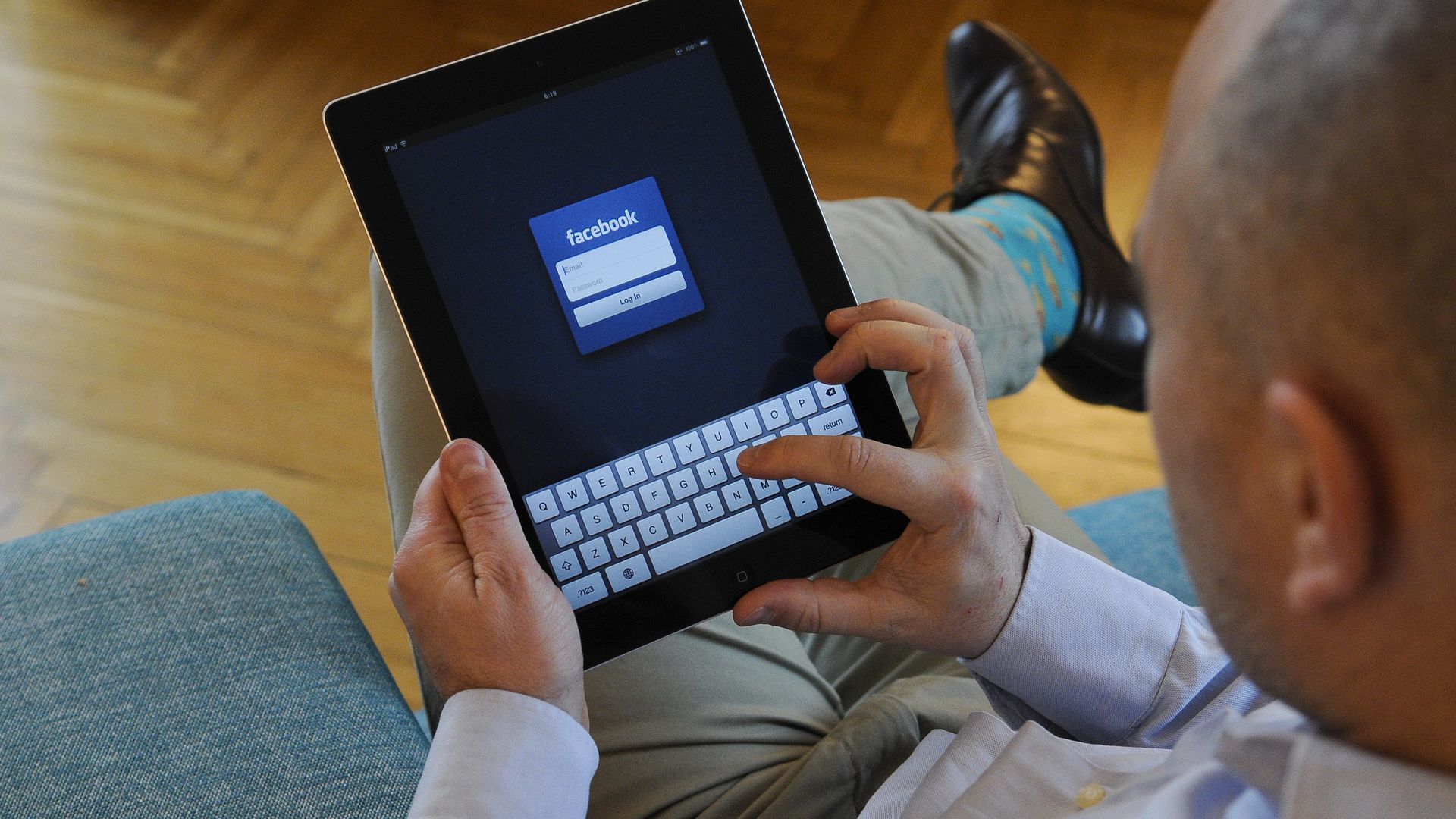 A man is seen holding an iPad with Facebook login screen.