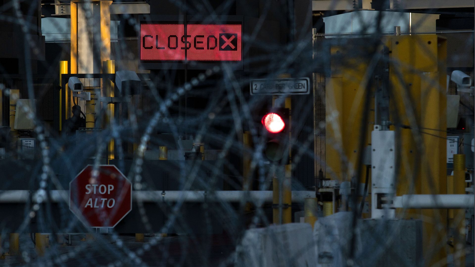 A photo through barbed wire of a port of entry with a "closed" sign 