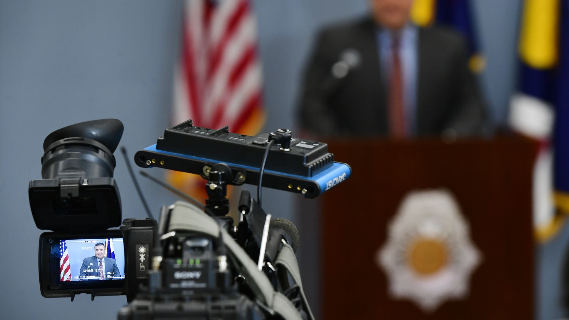 A camera pointed at a man speaking at a lectern.