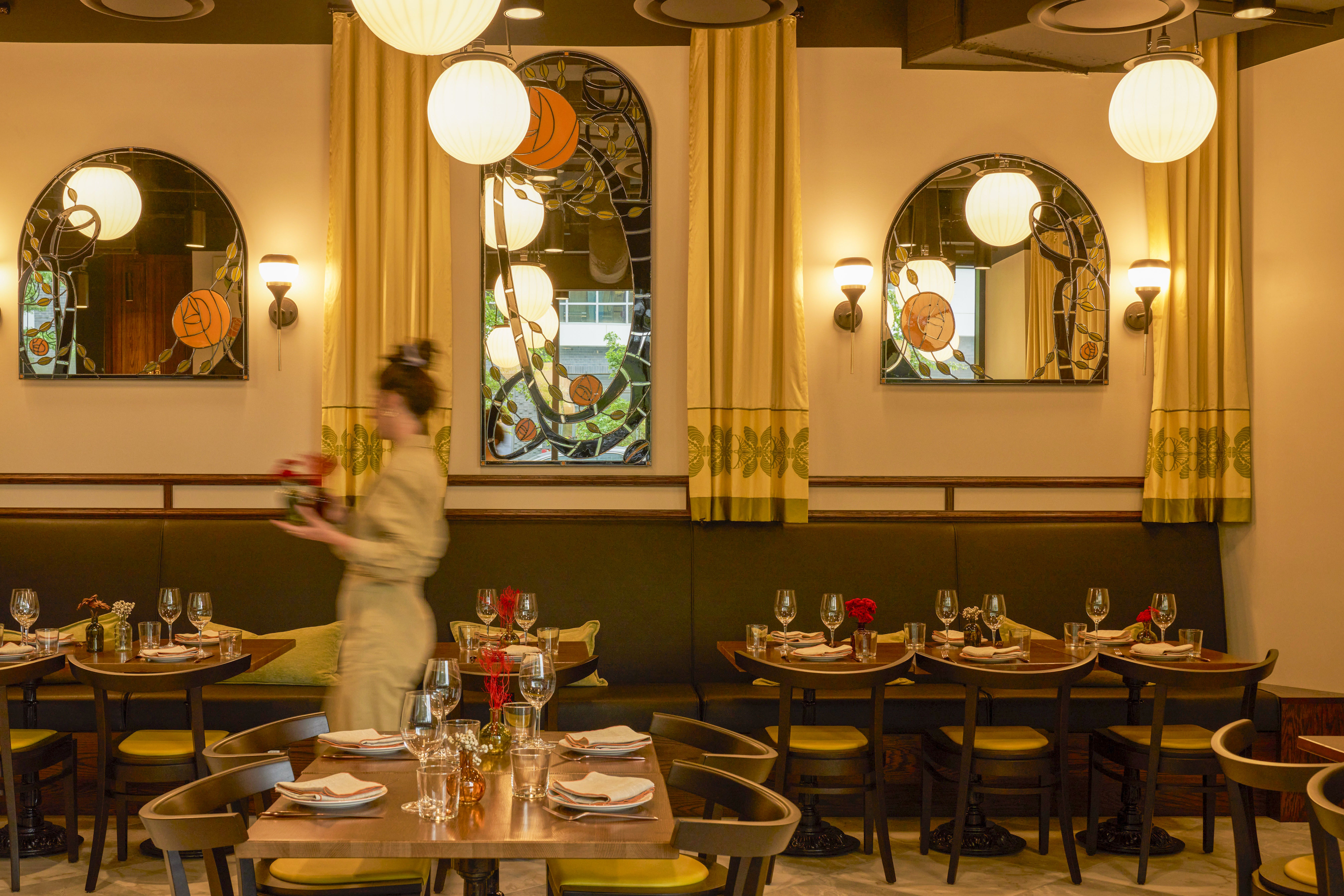 The dining room at Ama with yellow curtains and mirrors above wooden tables