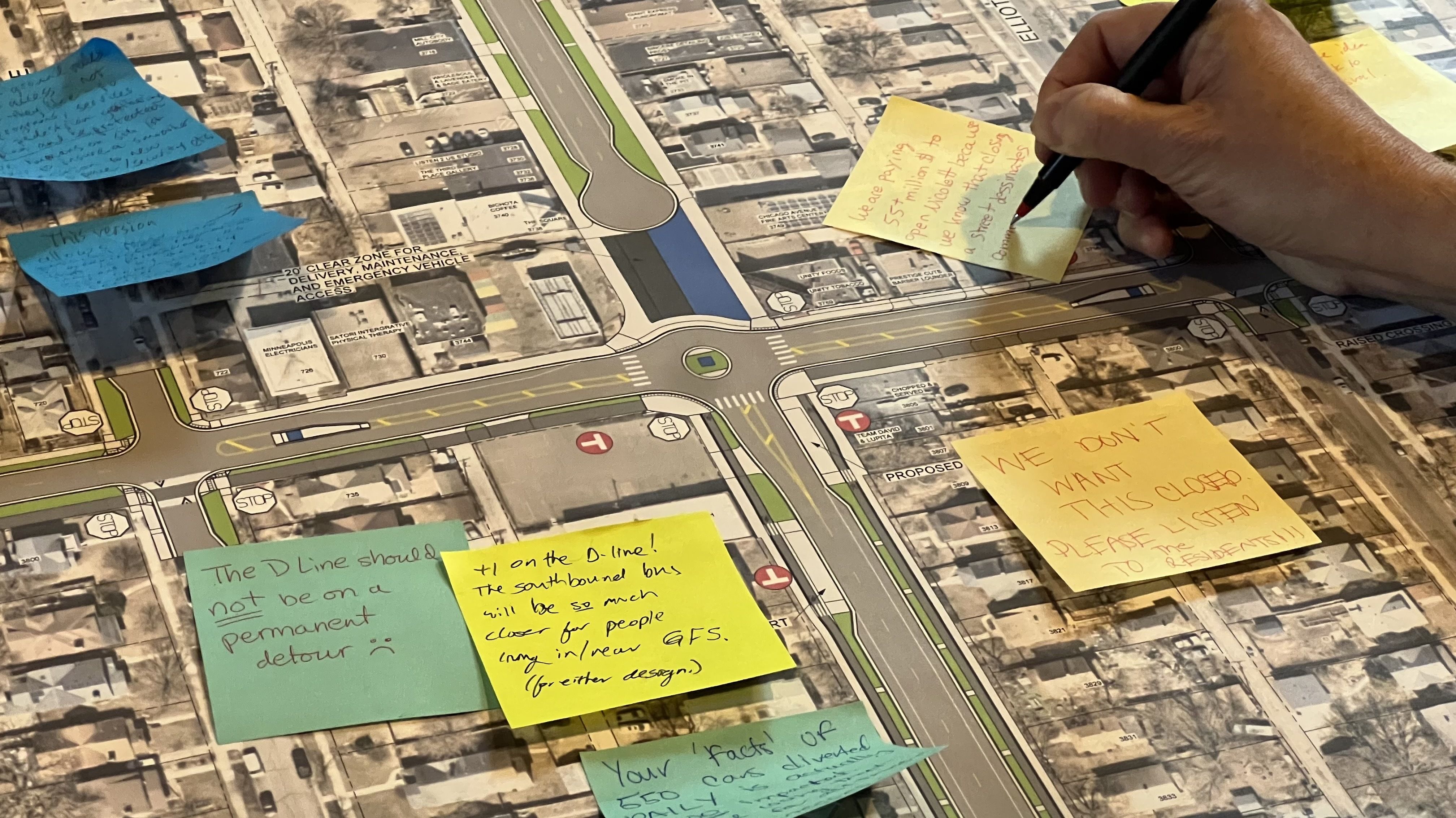 Hand writing on yellow sticky notes with community concerns on a detailed street map showing roads, buildings, and intersections, including notes about the D Line bus detour.