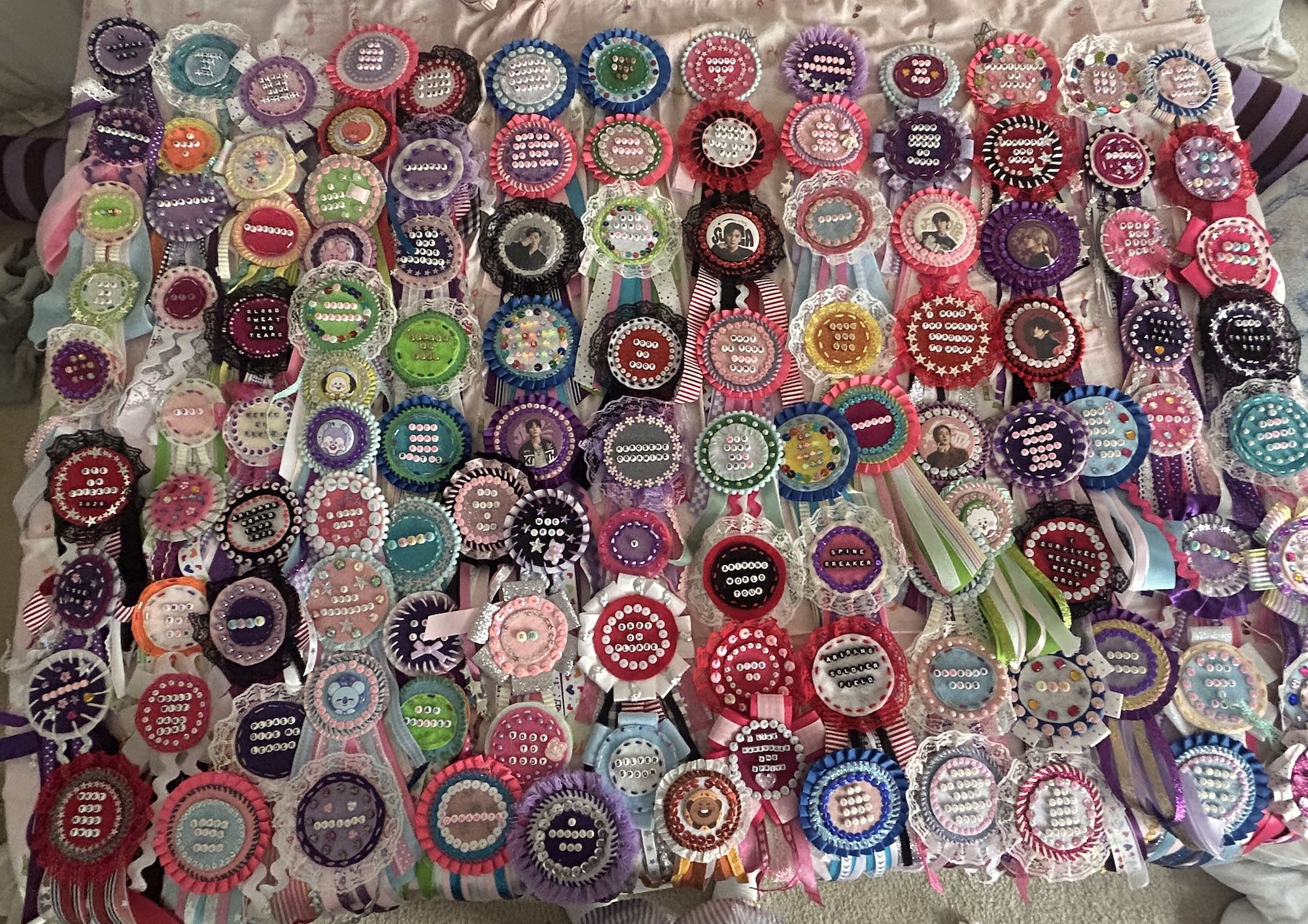 Many colorful handmade ribbon rosettes with lace borders and button centers, some featuring small photos or text in the center, arranged in rows on a fabric backdrop.
