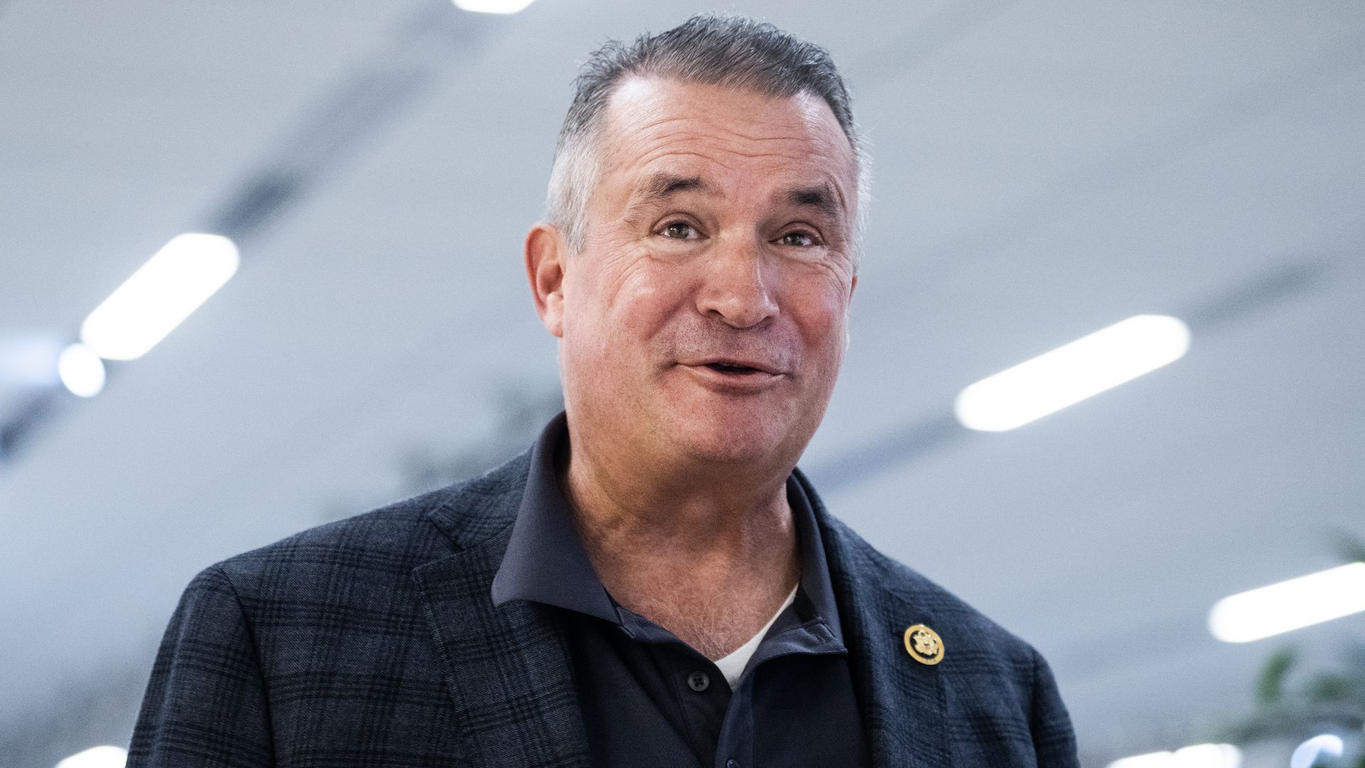 Rep. Don Bacon, wearing a dark blue suit, standing below a white ceiling.