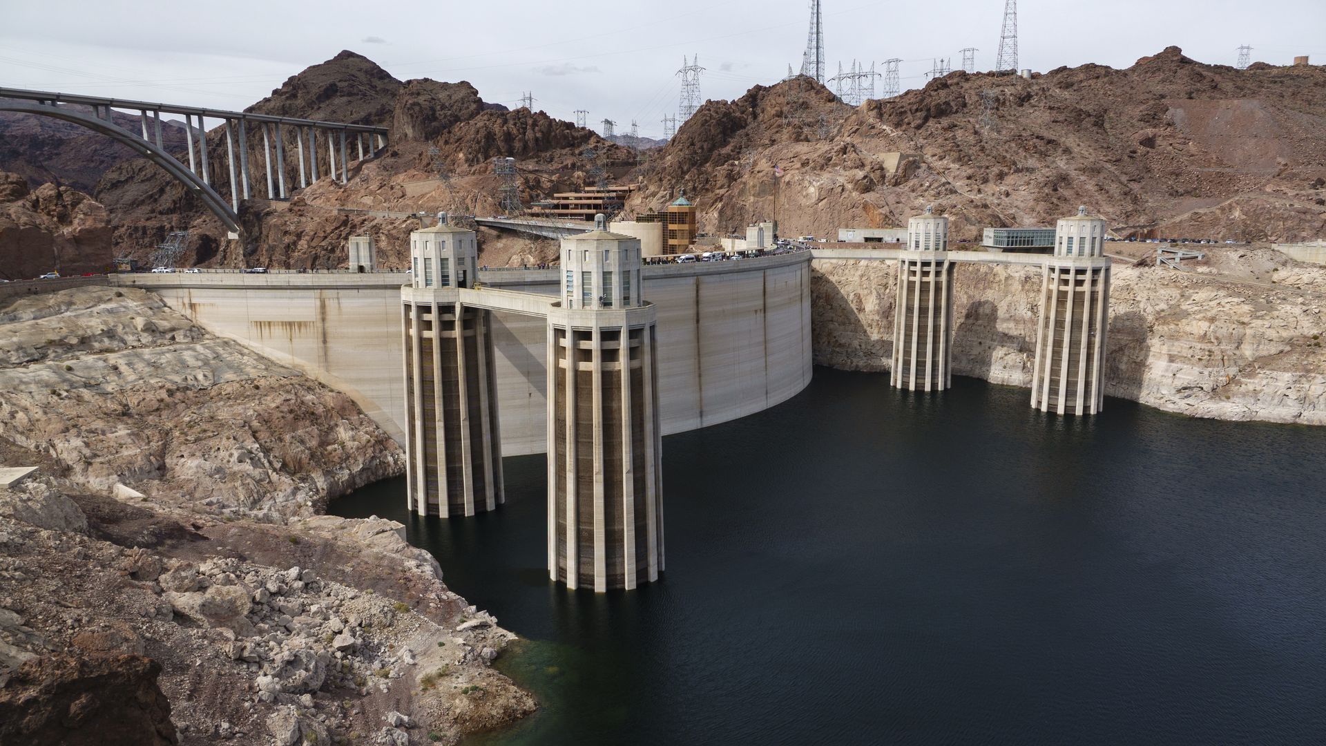 A river and dam with four large concrete pylons and a bridge in the mountainous background. 