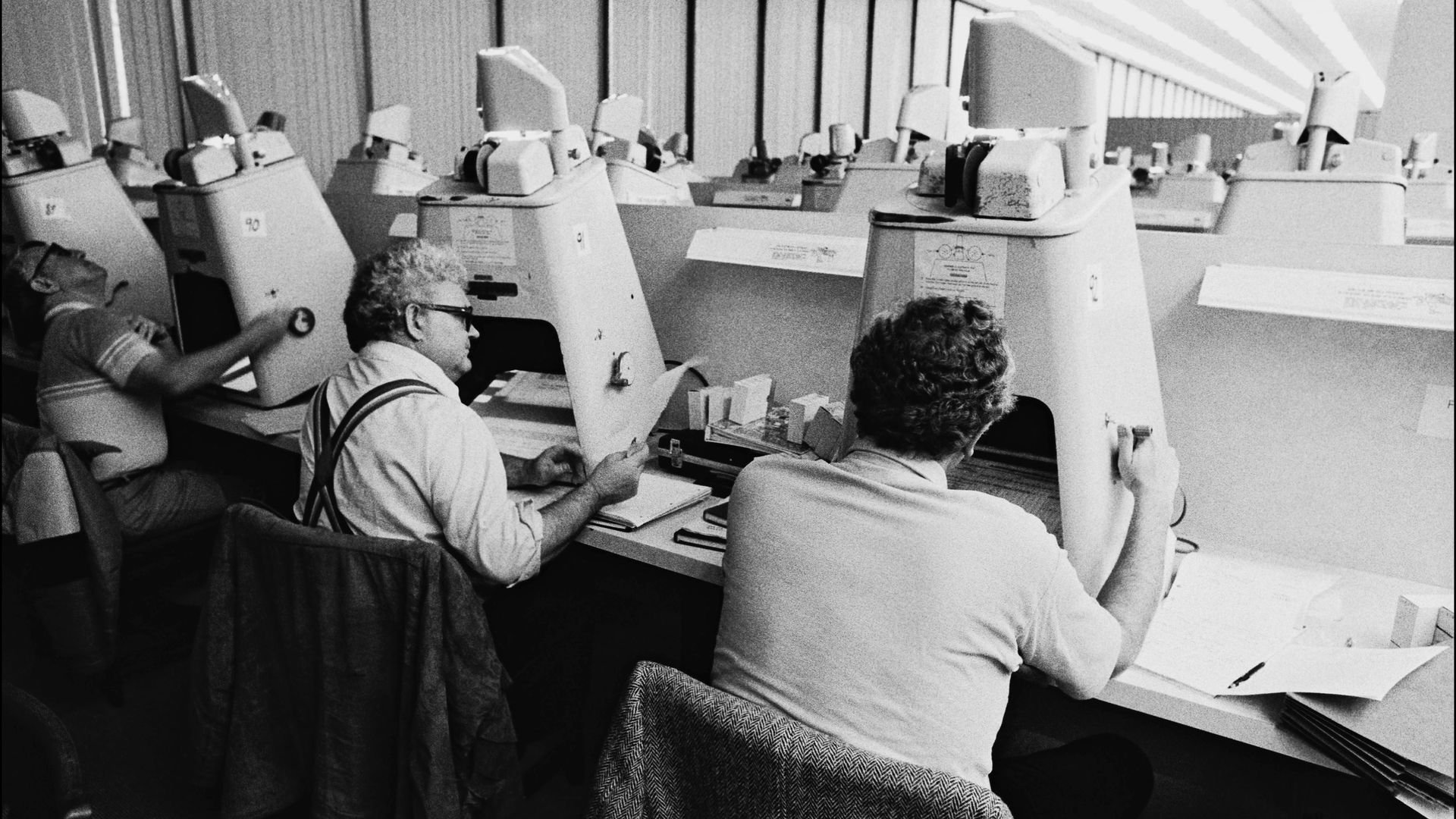 Black and white photo of men viewing documents on microfiche readers