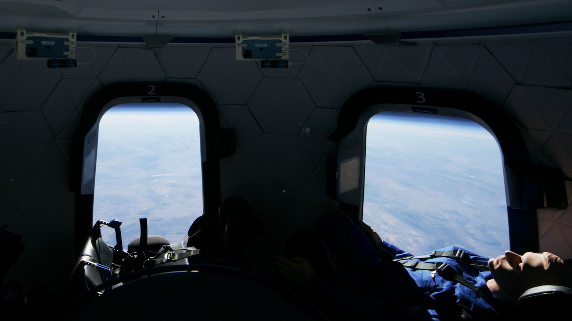 A test dummy inside a New Shepard capsule during a flight, with the blues of the Earth out a window