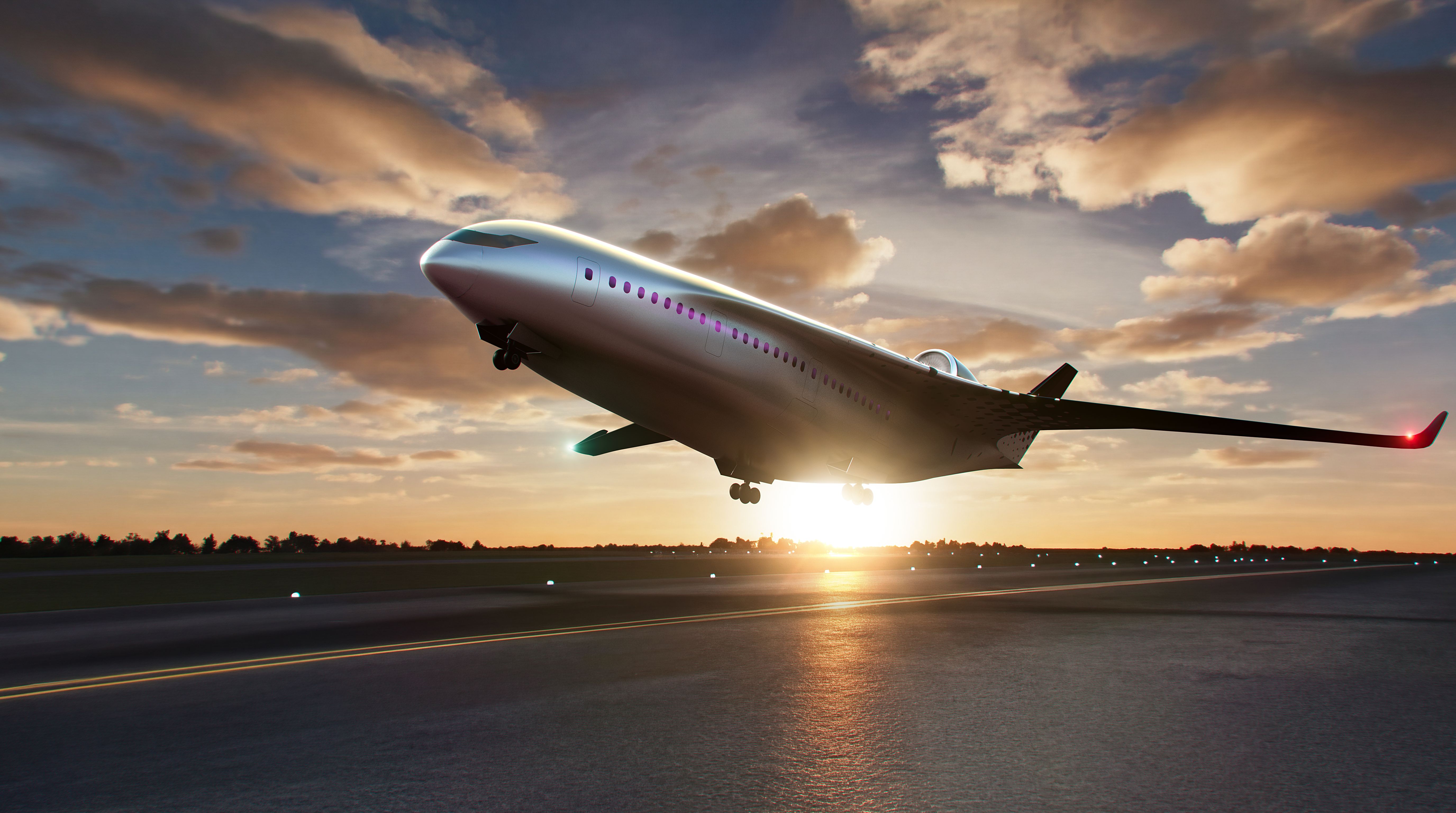 Silver passenger jet lifting off a runway at sunset, wheels still down. Long wings with a red-tipped winglet slice through an orange-pink sky, while runway lights glow below.