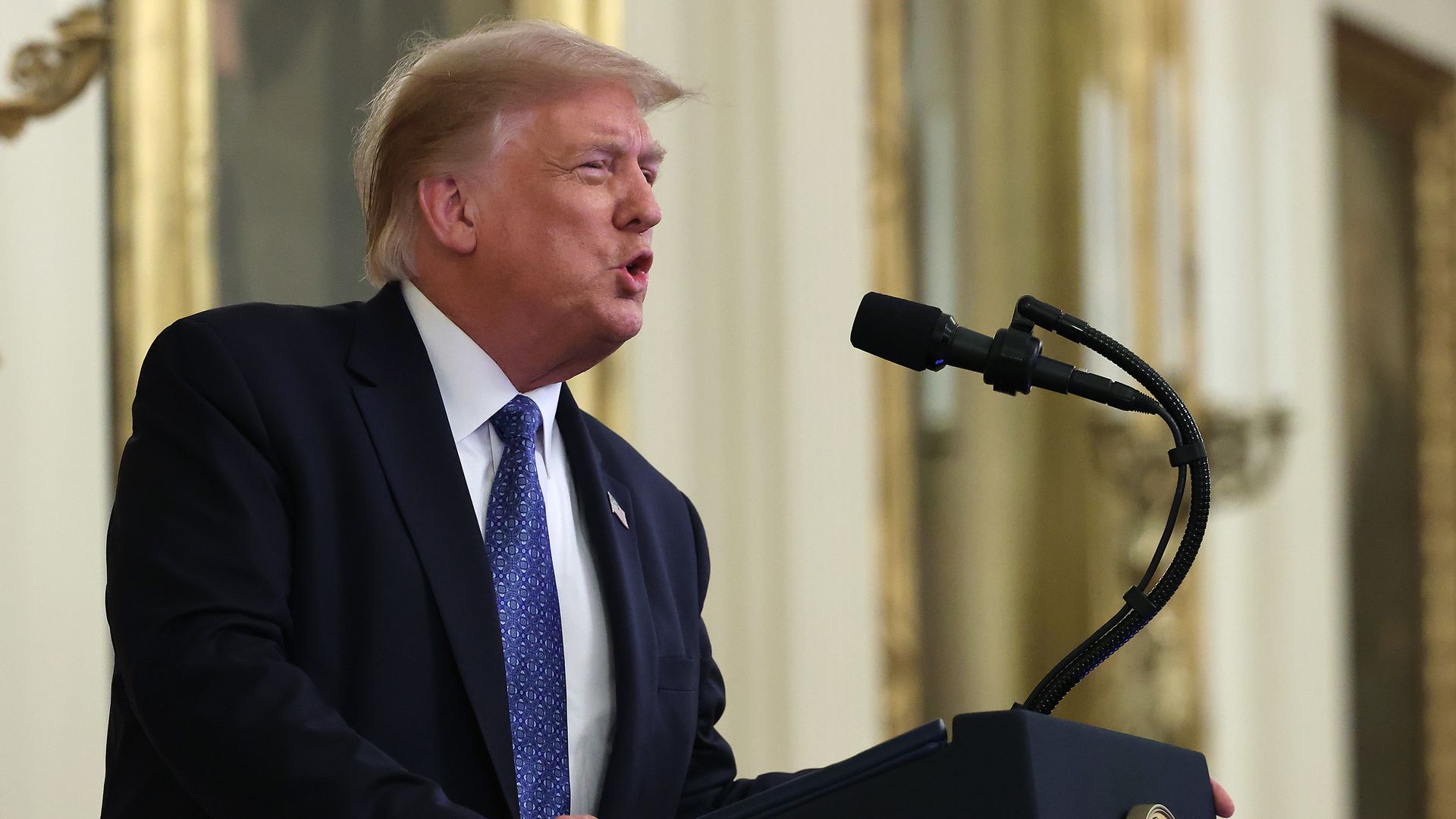 President Trump speaking into a mirophone at a podium with the presidential seal
