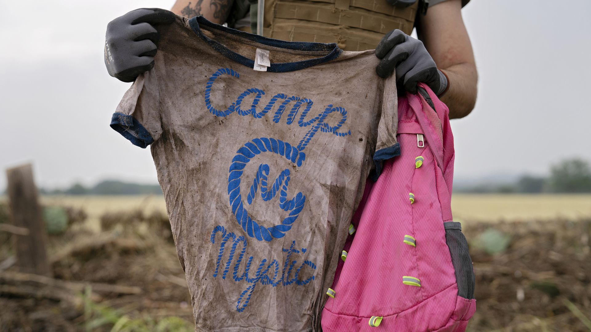 A search and rescue volunteer holds a dirty shirt that says "Camp Mystic" after floods in Texas.