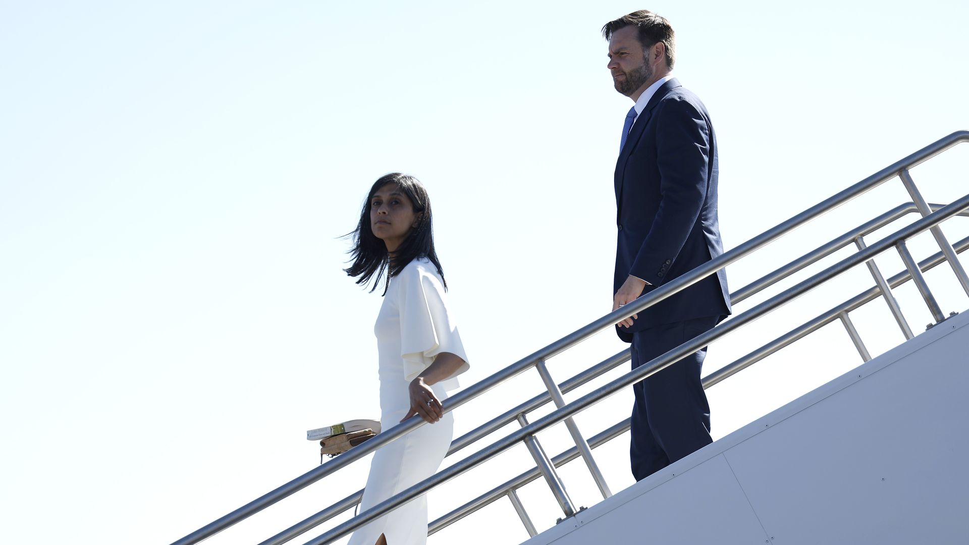 Usha and JD Vance go down the stairs outside of a plane.