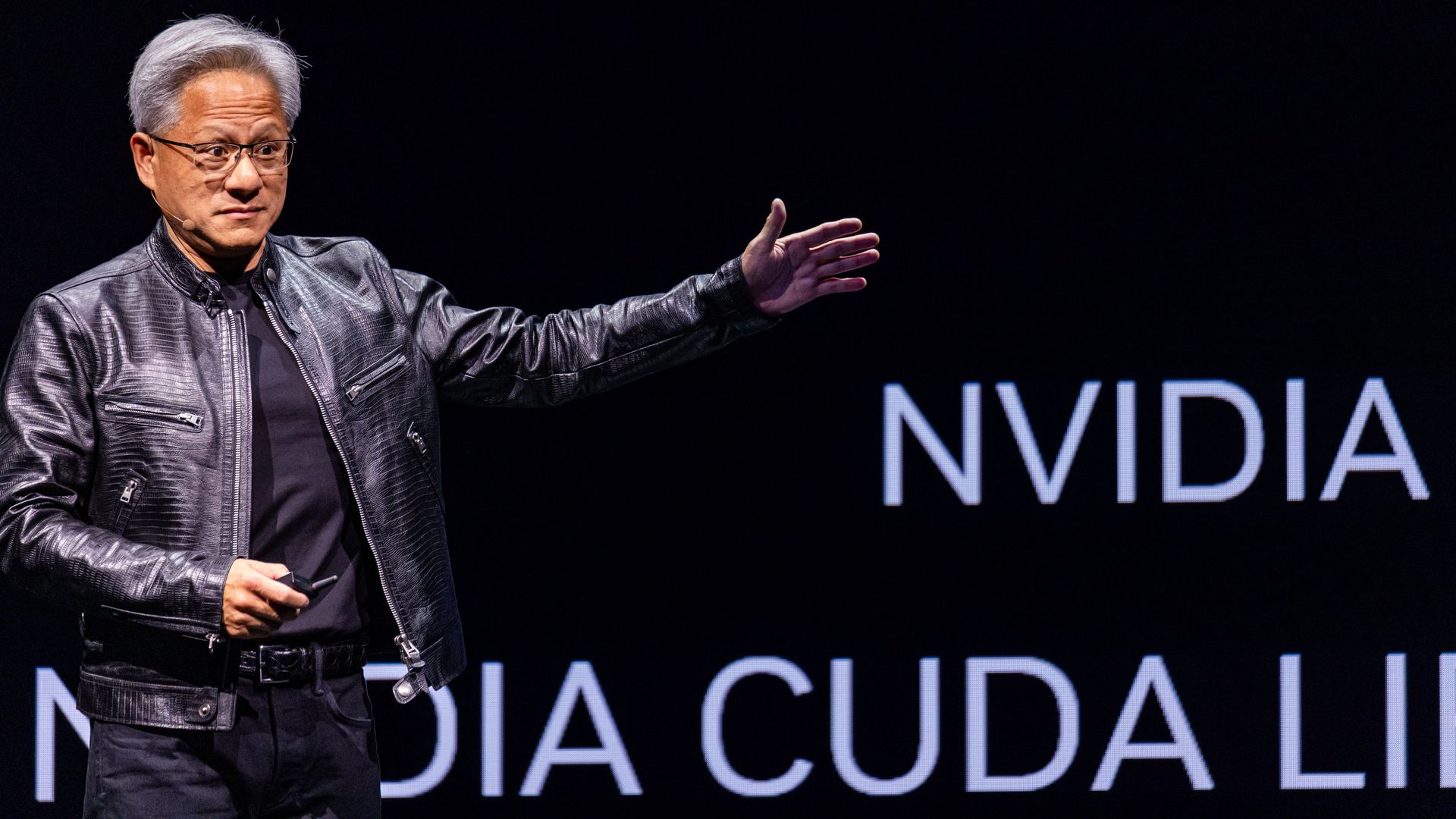 man in leather jacket holding his hand up on a stage