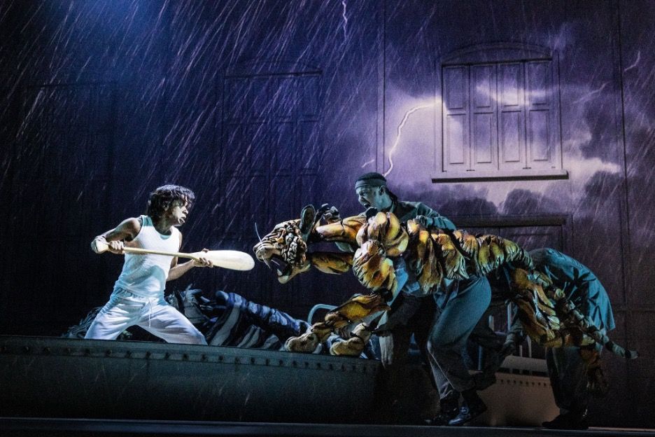 A scene from Life of Pi on a stage. A man is fighting off a pretend-tiger with an oar. 