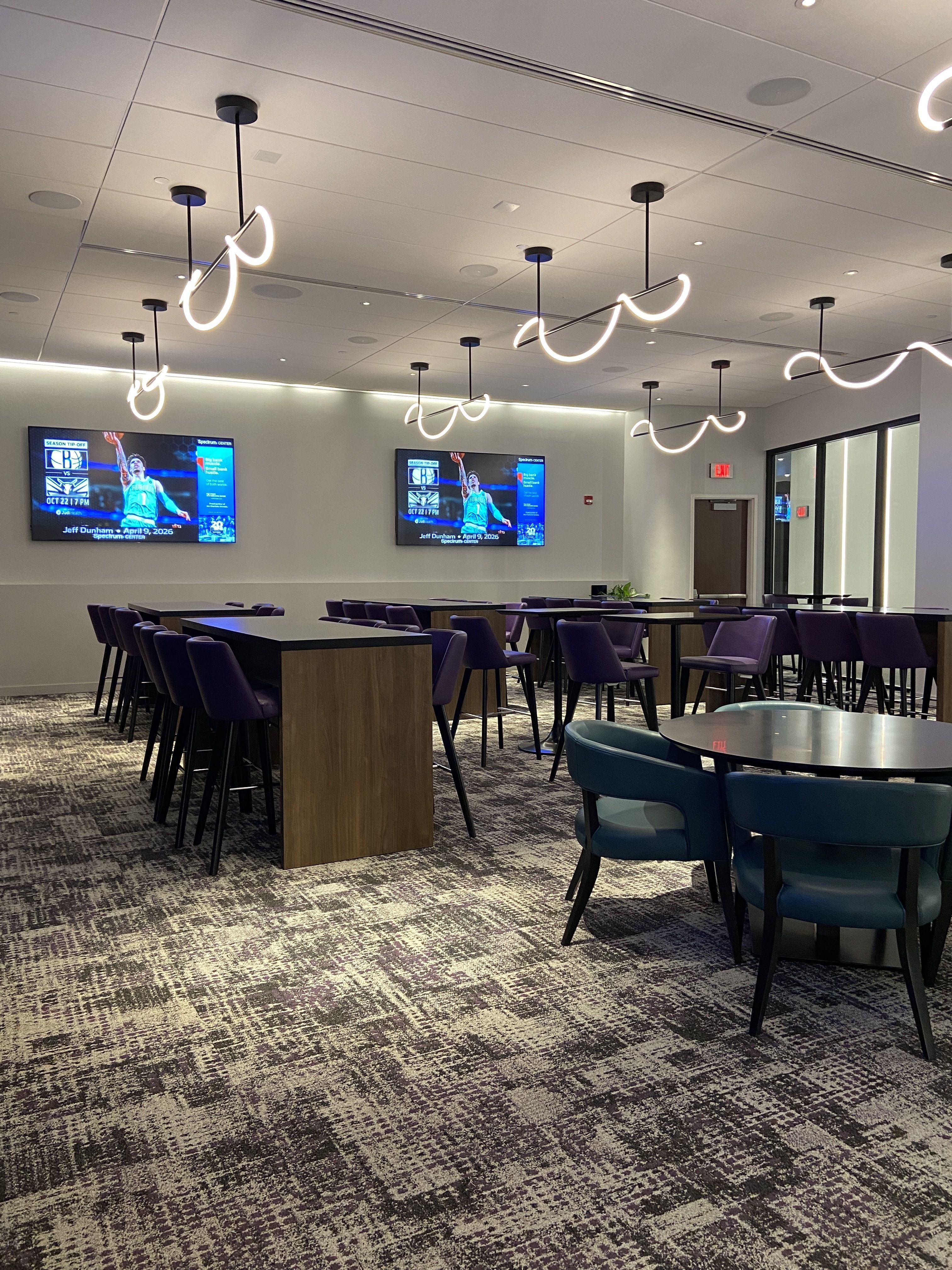 Inner Circle Club is a modern lounge area with purple chairs around black tables, patterned carpet, abstract ceiling lights, two TVs on the wall showing sports ads, and glass door entrance.