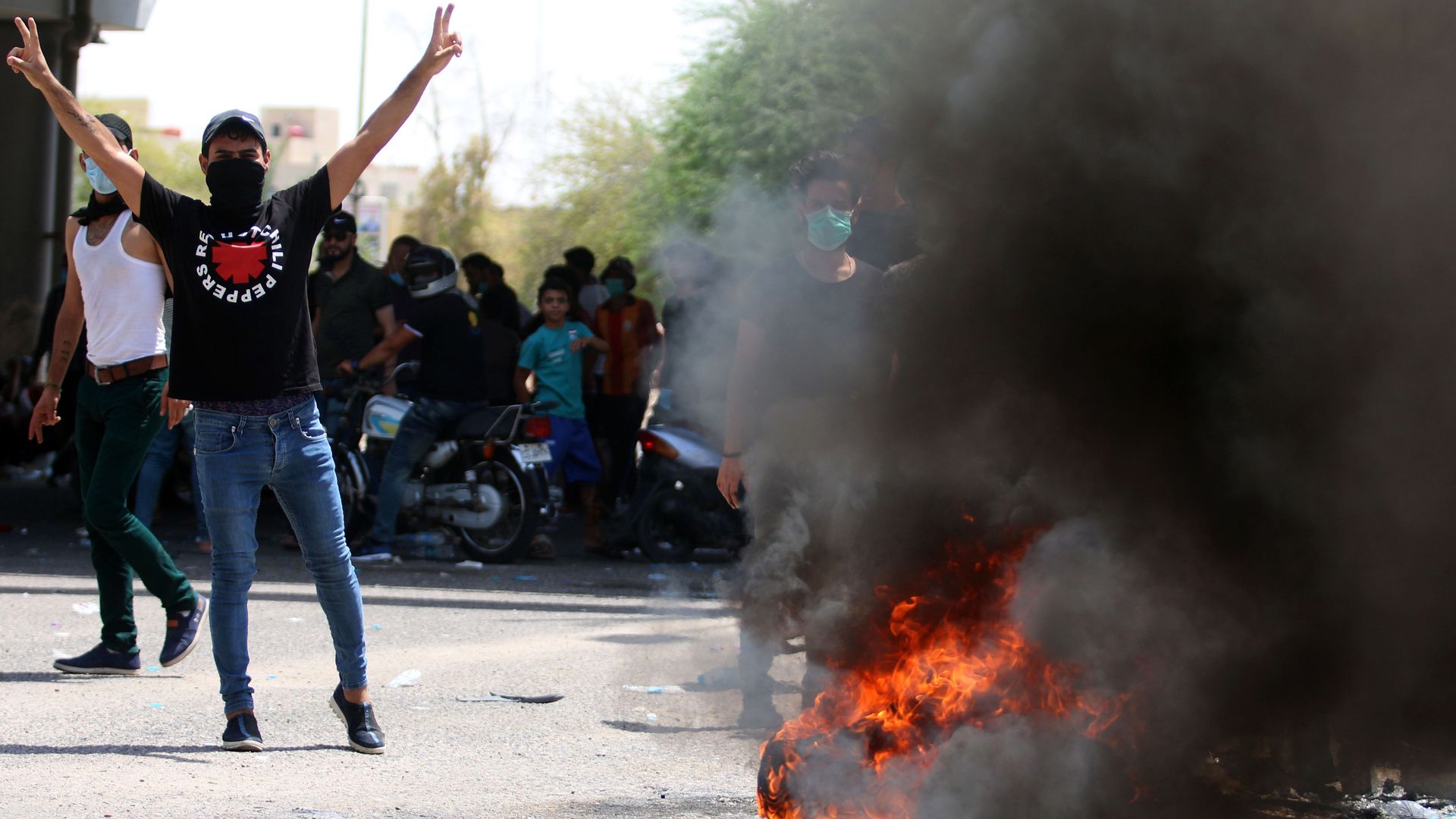A protestor stands next to a burning tire, with his hands raised gesturing the peace sign. 