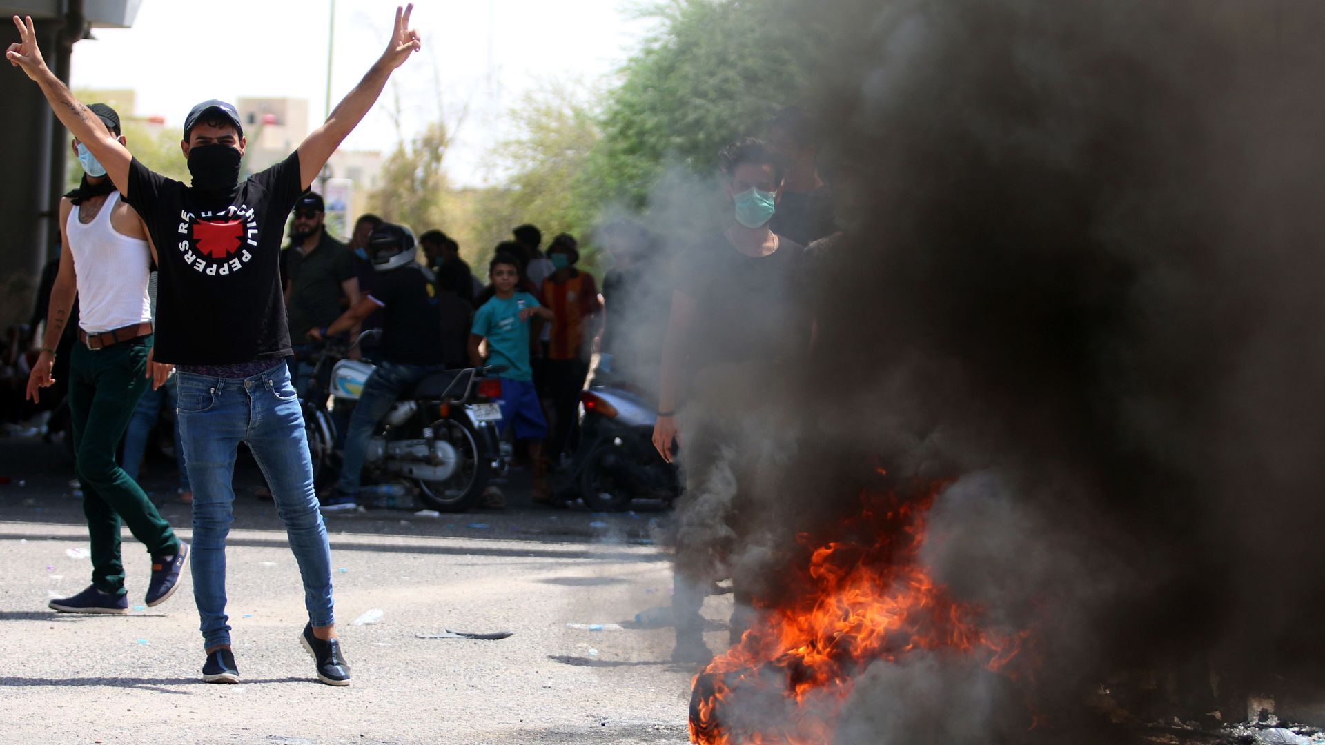 A protestor stands next to a burning tire, with his hands raised gesturing the peace sign.
