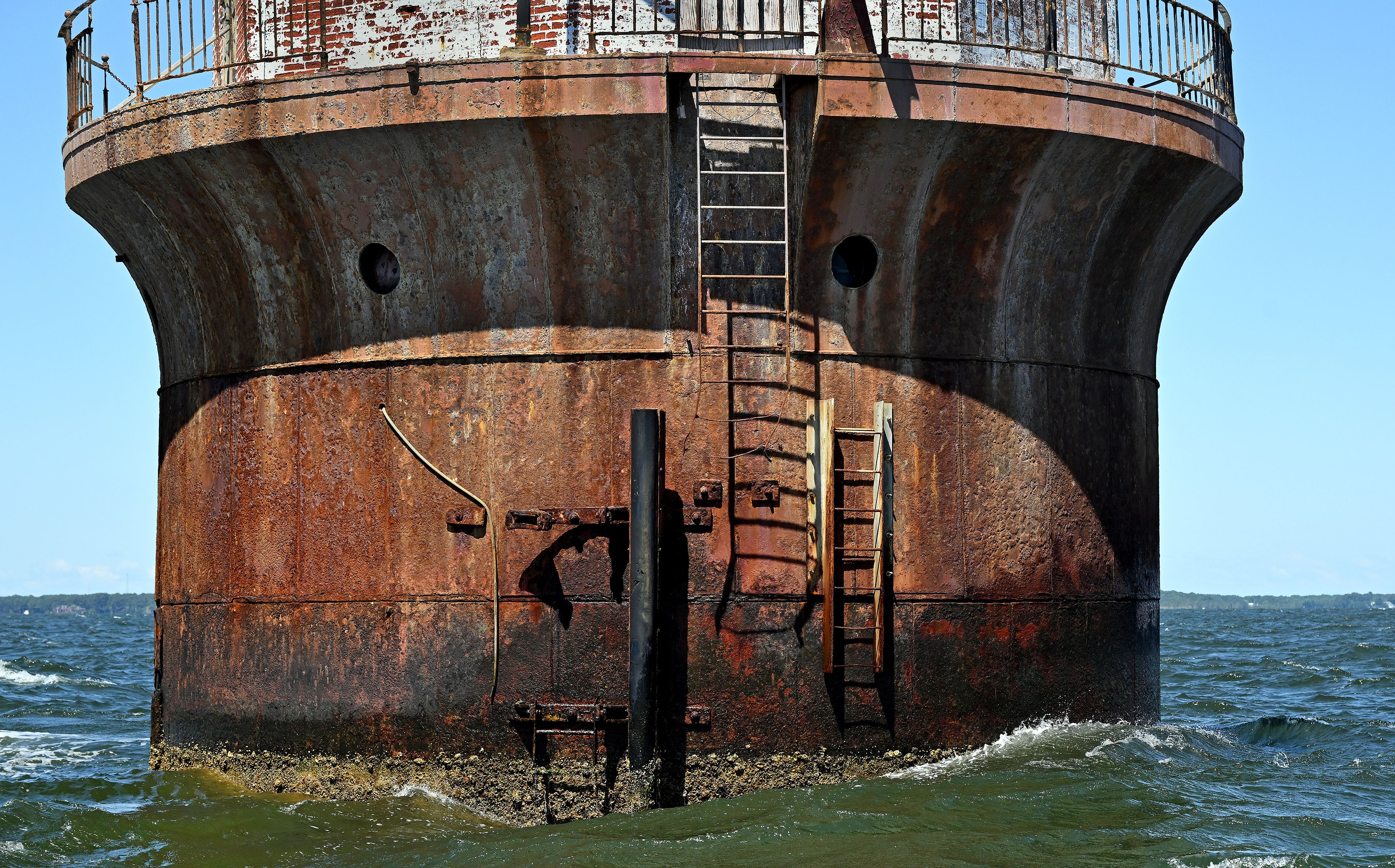 A rusty steel ladder at the bottom of a lighthouse surrounded by water