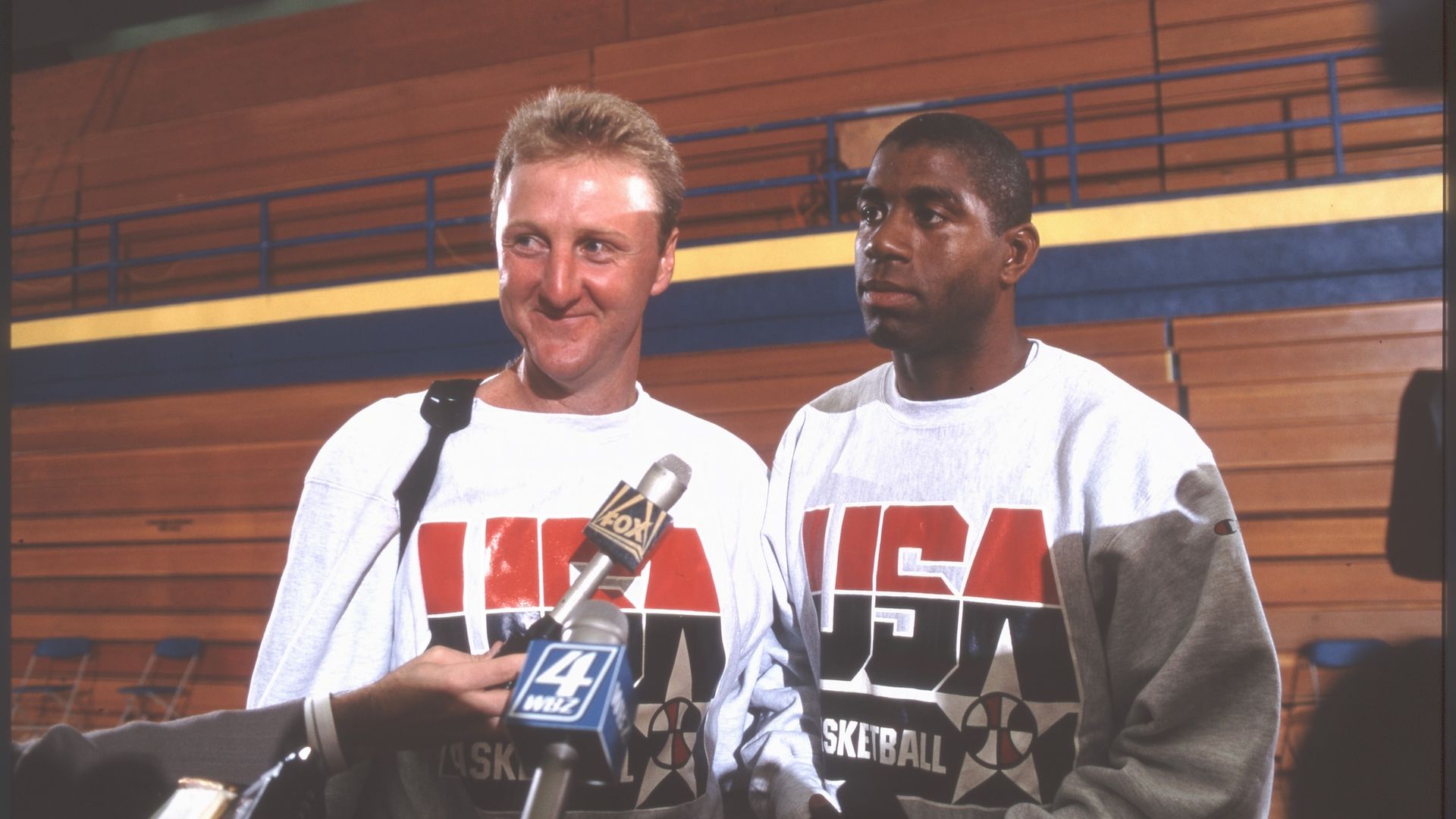 Larry Bird and Magic Johnson of Team USA stand in front of bleachers answering questions from media in 1992.