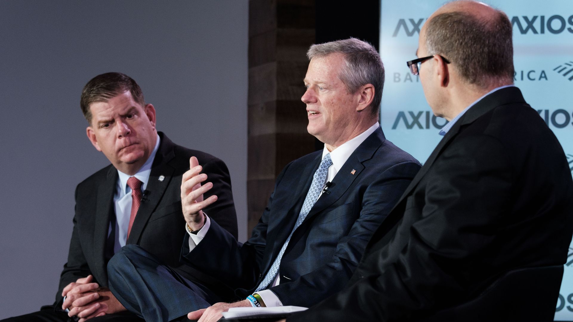 Three men sit on Axios stage for event.