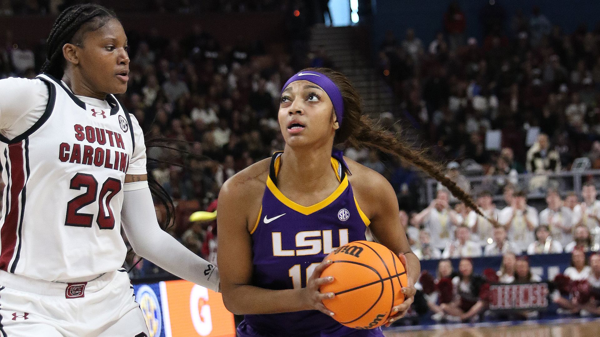 Angel Reese looks to score while holding a basketball. A South Carolina player approaches to attempt to block her.