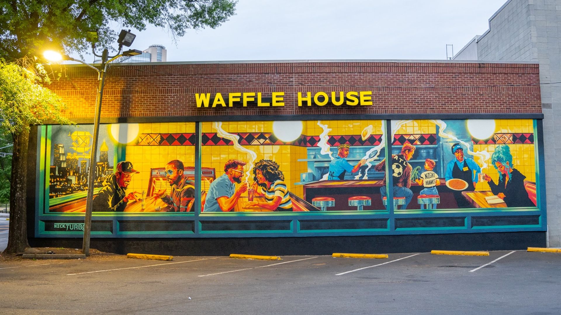 Bright Waffle House storefront with a bold yellow sign on a red brick wall; mural windows depict a retro diner scene with people eating, steaming coffee, and neon-tinted interiors.