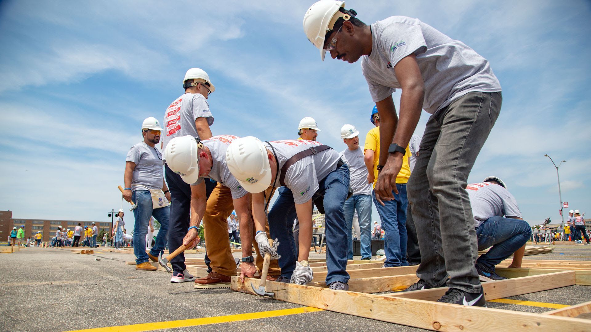 Workers nail pieces of wood in a parking lot.