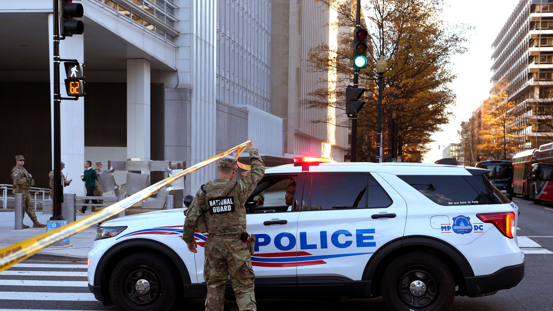 Members of the National Guard holding caution tape in front of a police vehicle