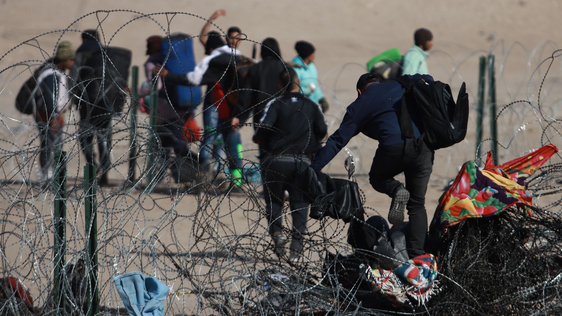 migrants are shown from behind walking among razor wire near the US/MEXICO border