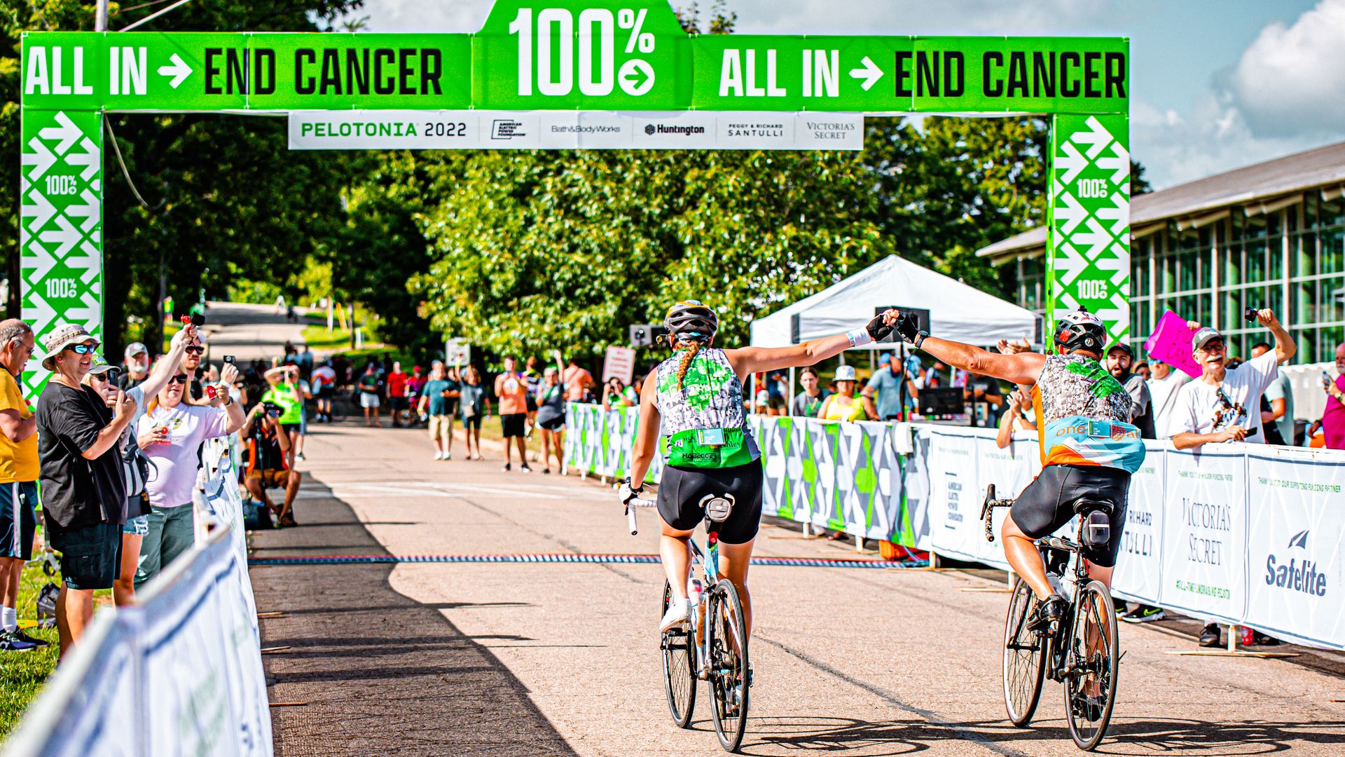 Two bicyclists fist-bump as they approach the bright green Pelotonia finish line
