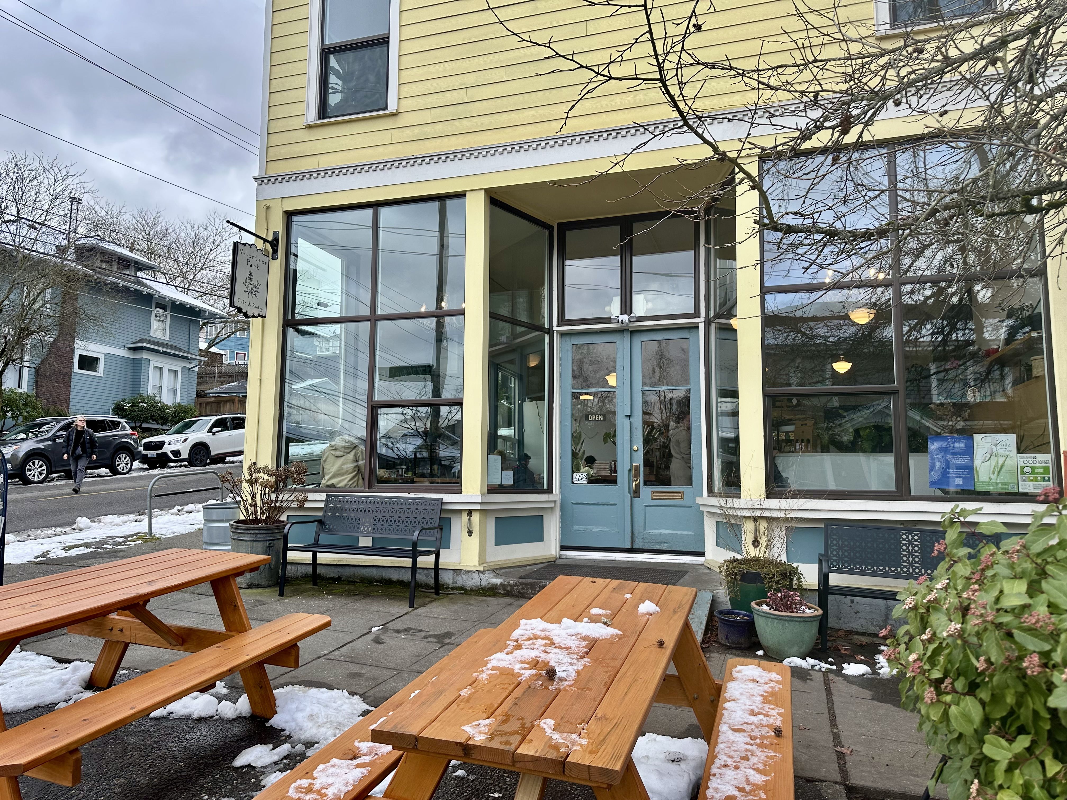 The front of Volunteer Park Cafe, with picnic tables on the sidewalk, a teal-colored door and yellow painted siding.