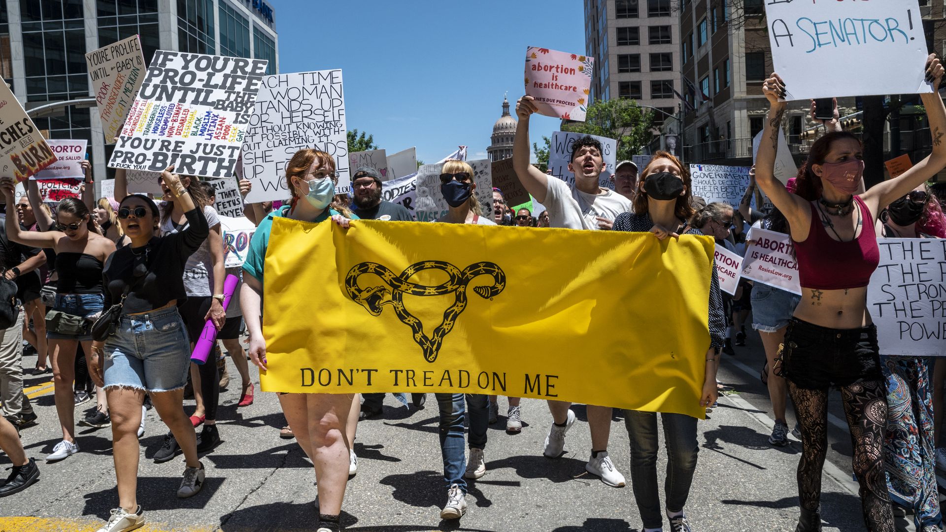 Photo of a crowd of pro-abortion protesters waving signs and a yellow banner that says "Don't tread on me"