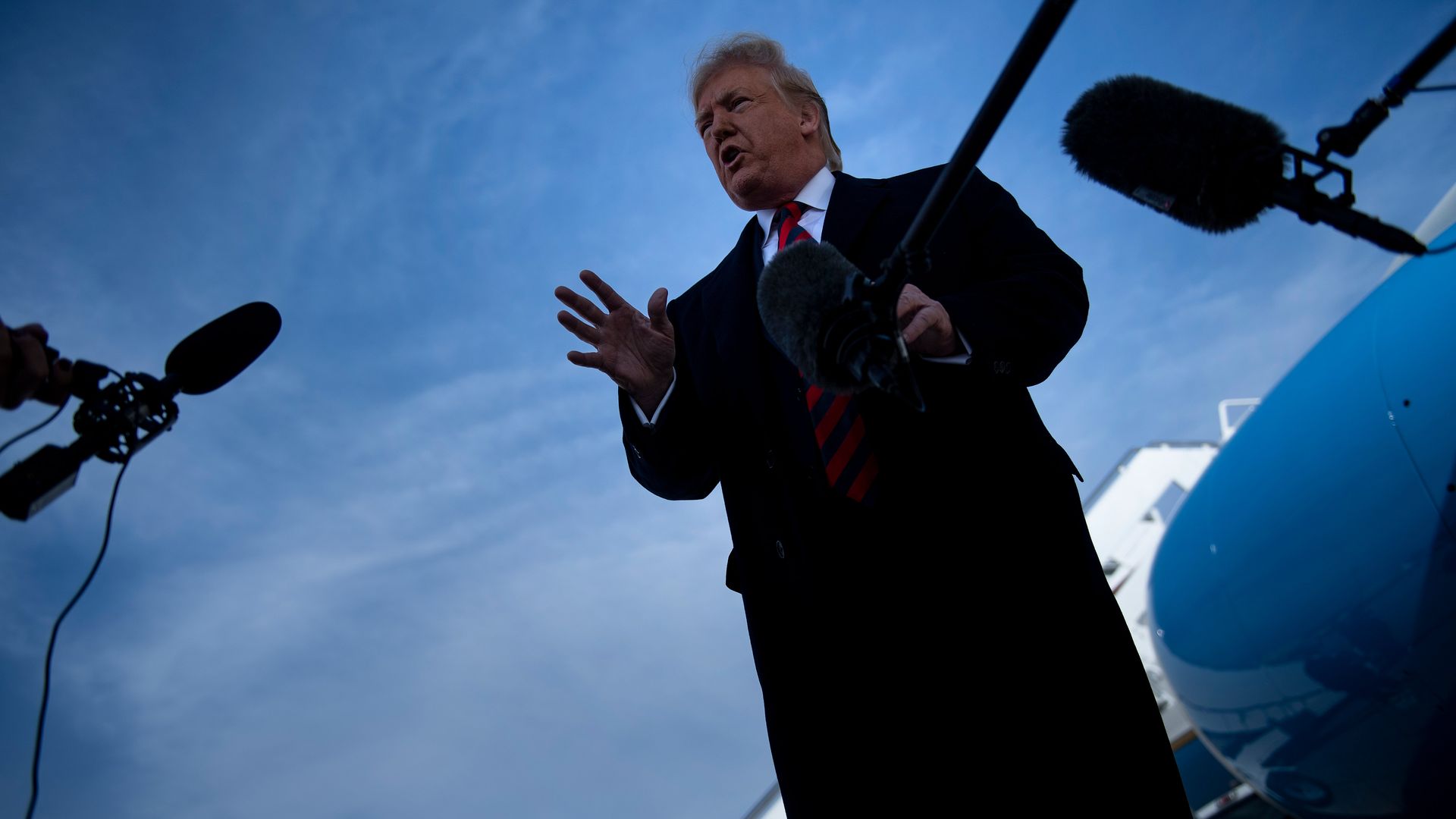 In this image, Trump stands in front of Air Force One and speaks into microphones.