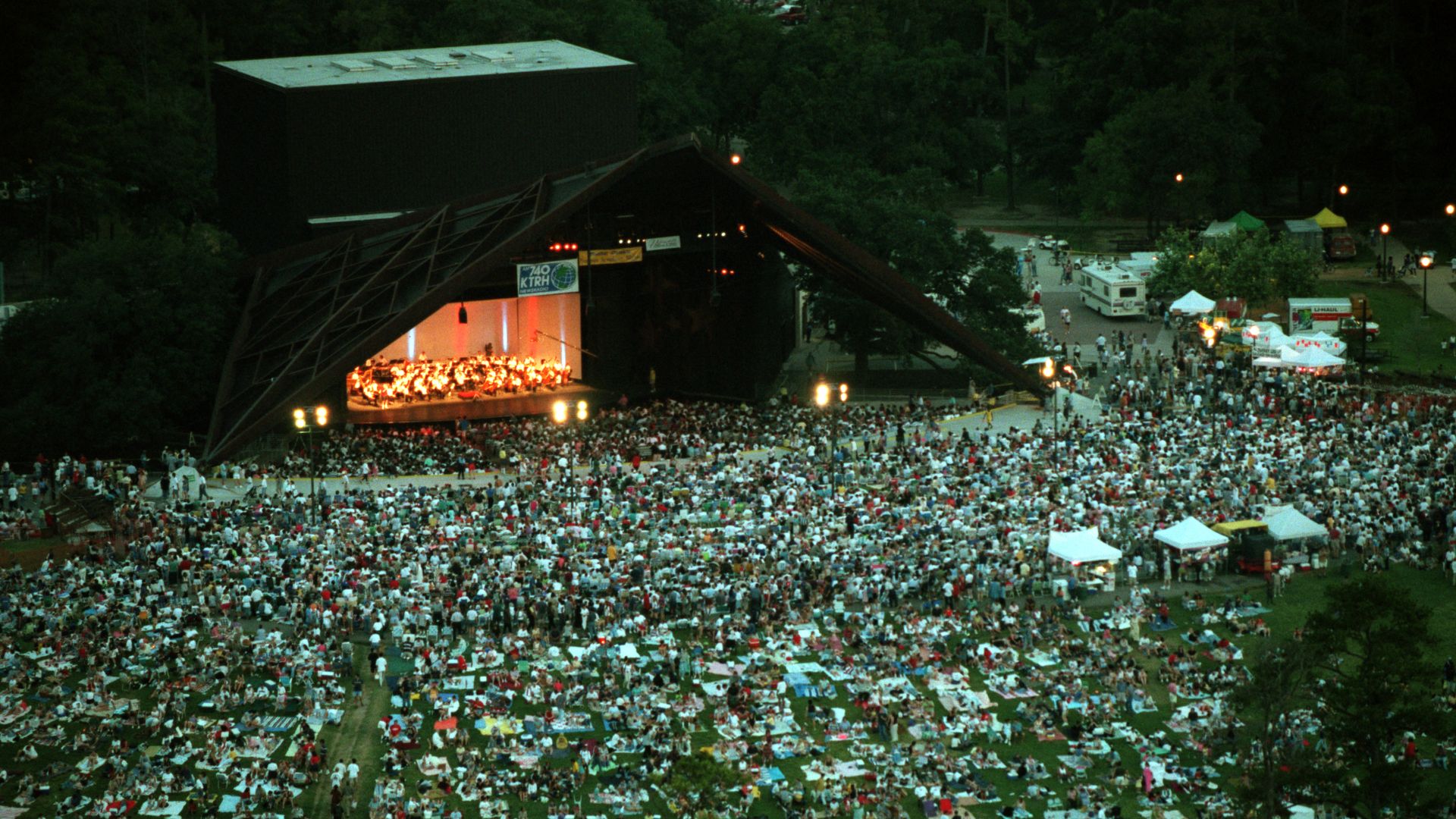 A large crowd of people with picnic blankets in front of an outdoor theater. 