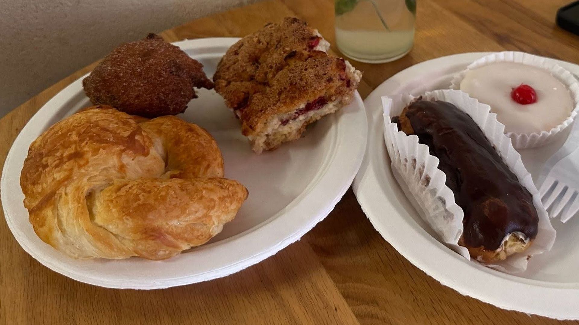 Table with croissants and pastries, a glass vase of red carnations, and neon yellow sunglasses on the right, against a textured white wall.