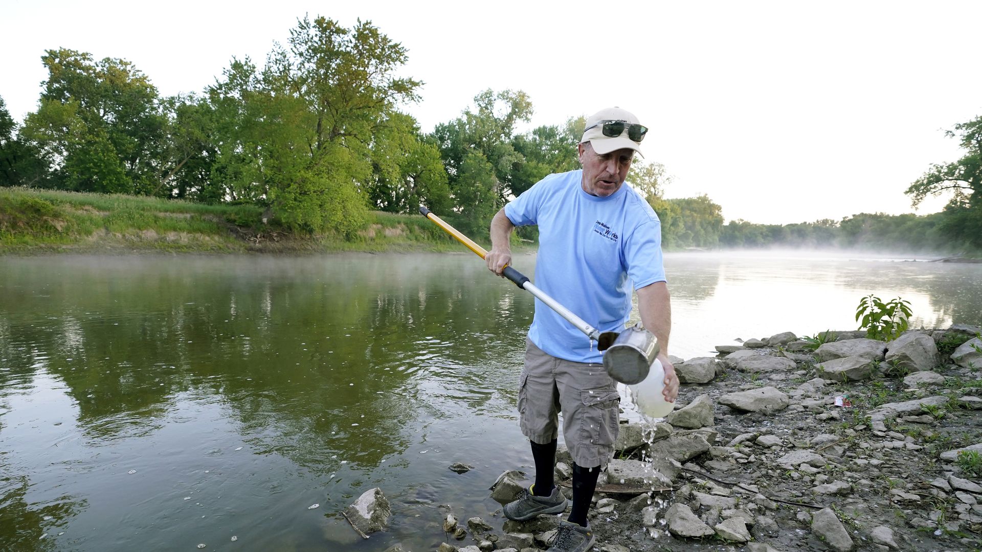 A photo of a man taking a water sample from a Des Moines river.