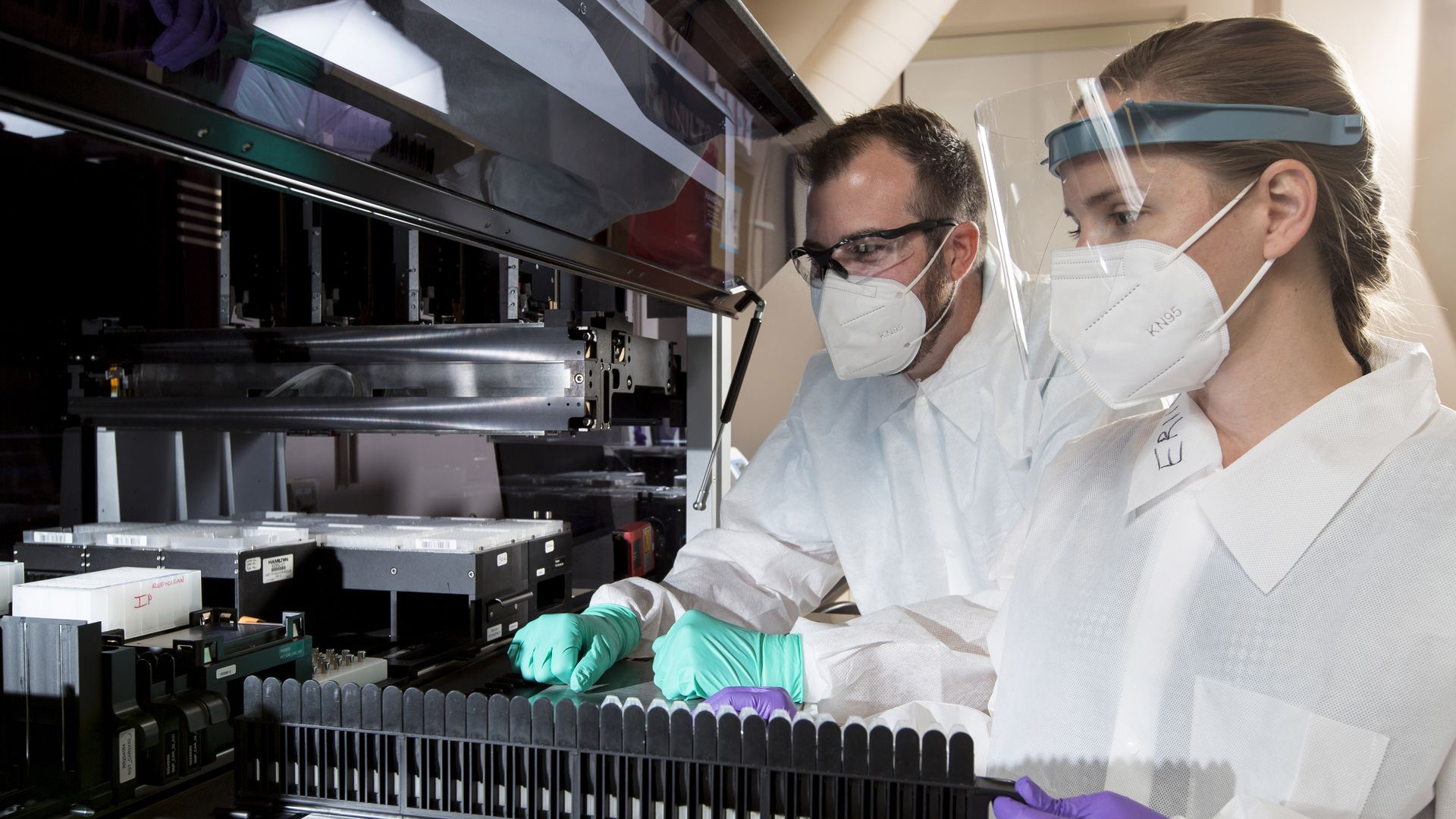Photo of two masked scientists looking at a row of beakers