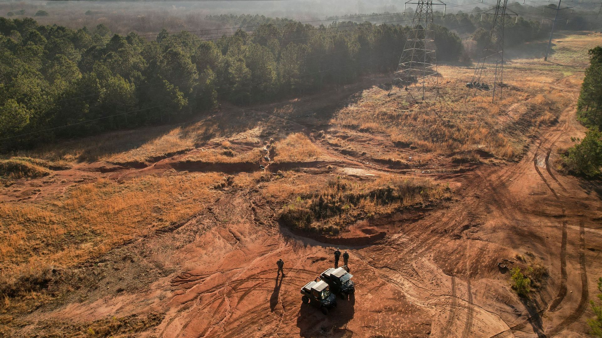 An aerial image of a police vehicle parked on a cleared rolling area bordered by a forest