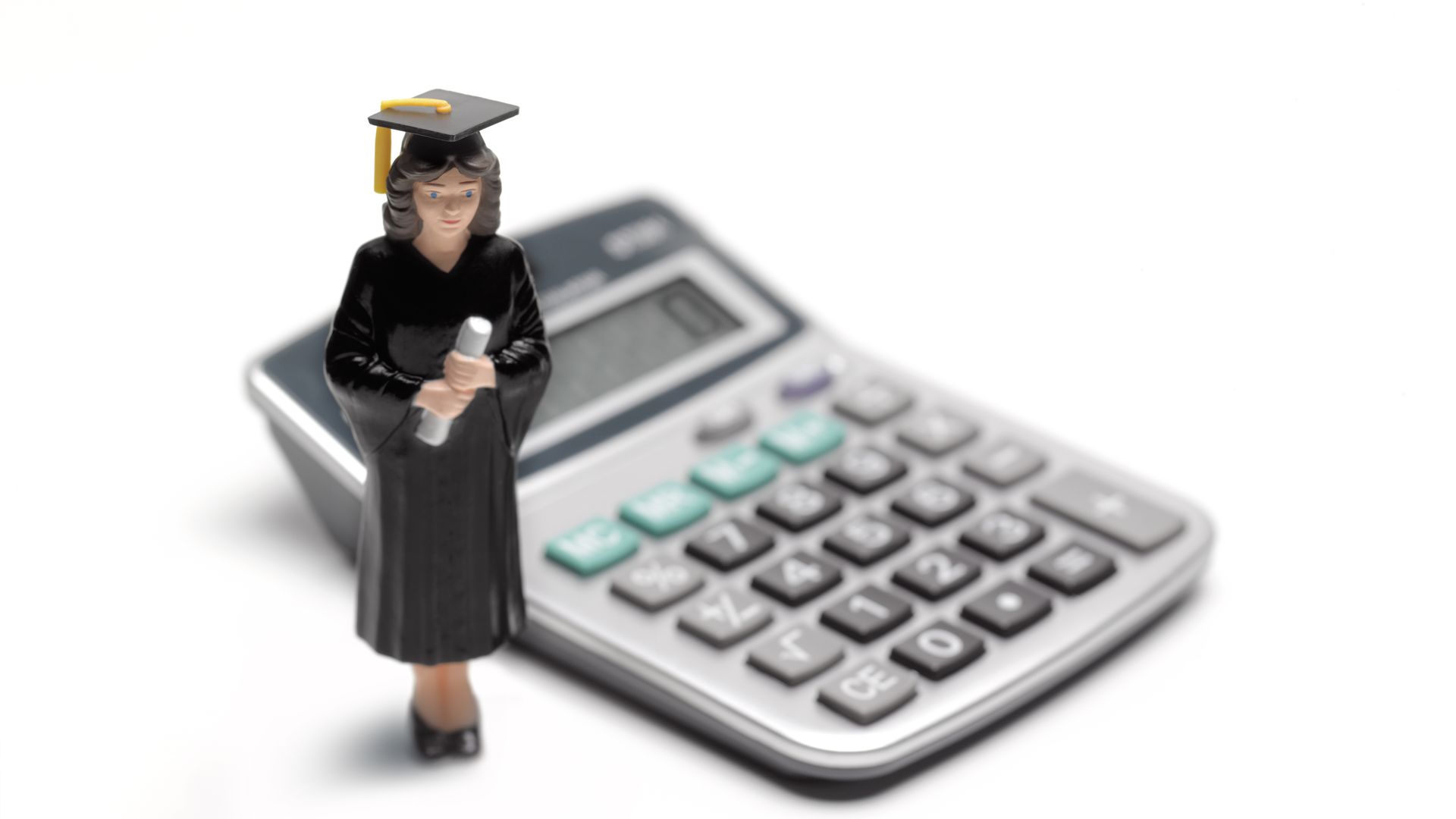 Student figurine in a graduation cap and gown standing next to a calculator  