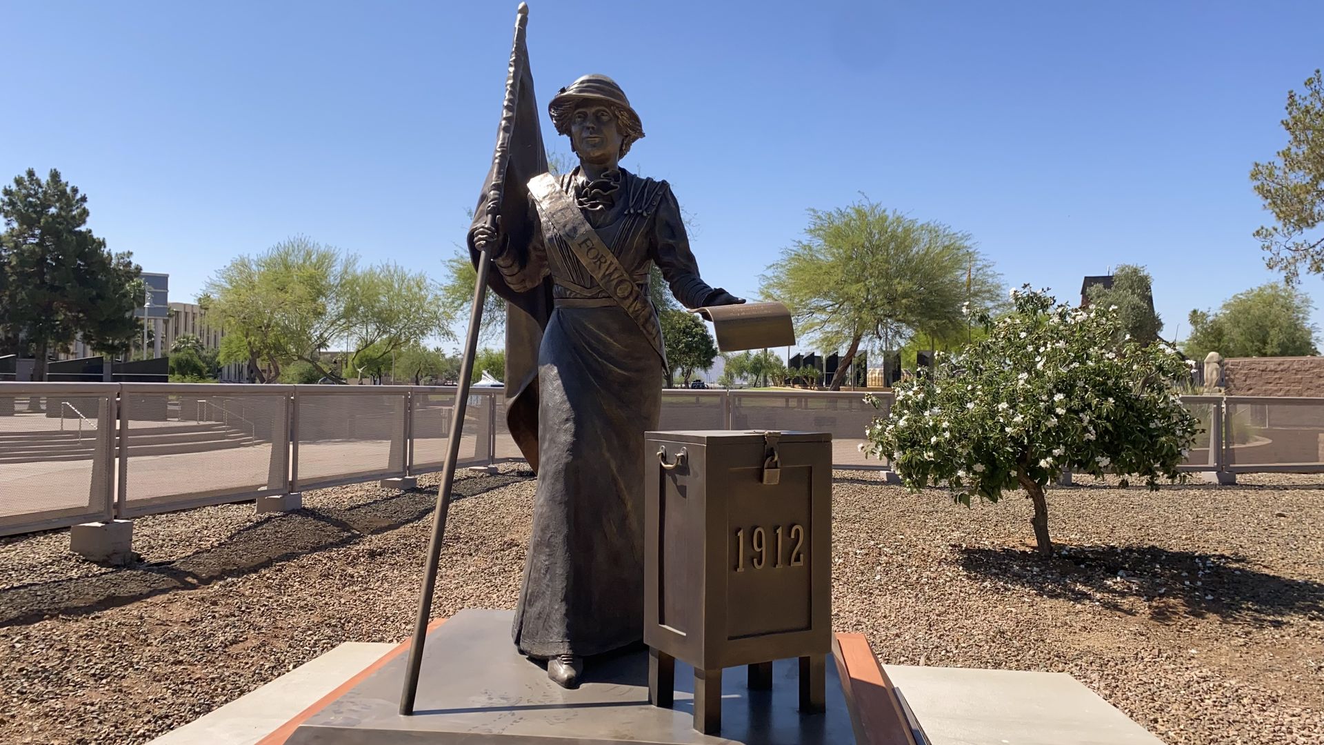 A bronze statue of a woman holding a flag and a piece of paper next to a box that says 1912.