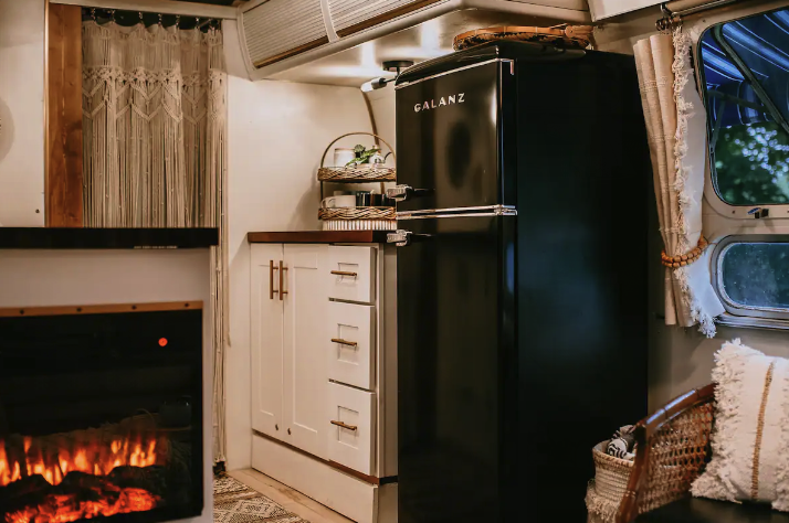 The interior of an Airstream camper with an electric fireplace and vintage refrigerator.