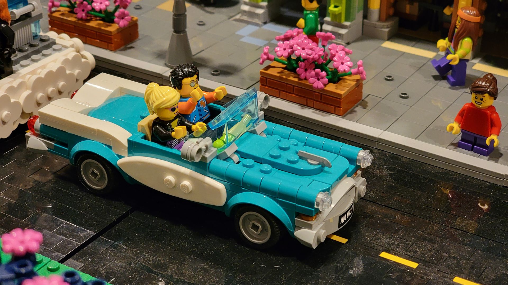 A blue Lego car with two Lego people inside driving on a street made of Legos