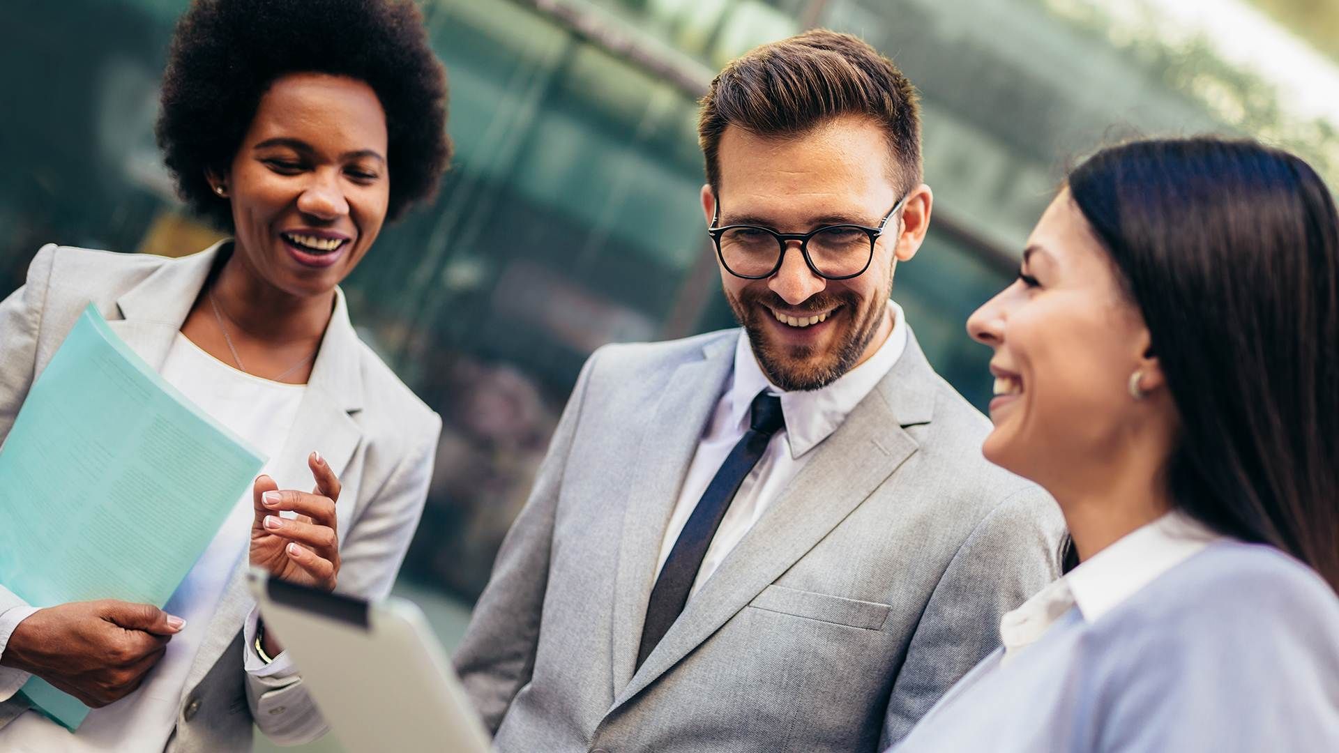 Two women and a man wearing business suits. They are laughing.