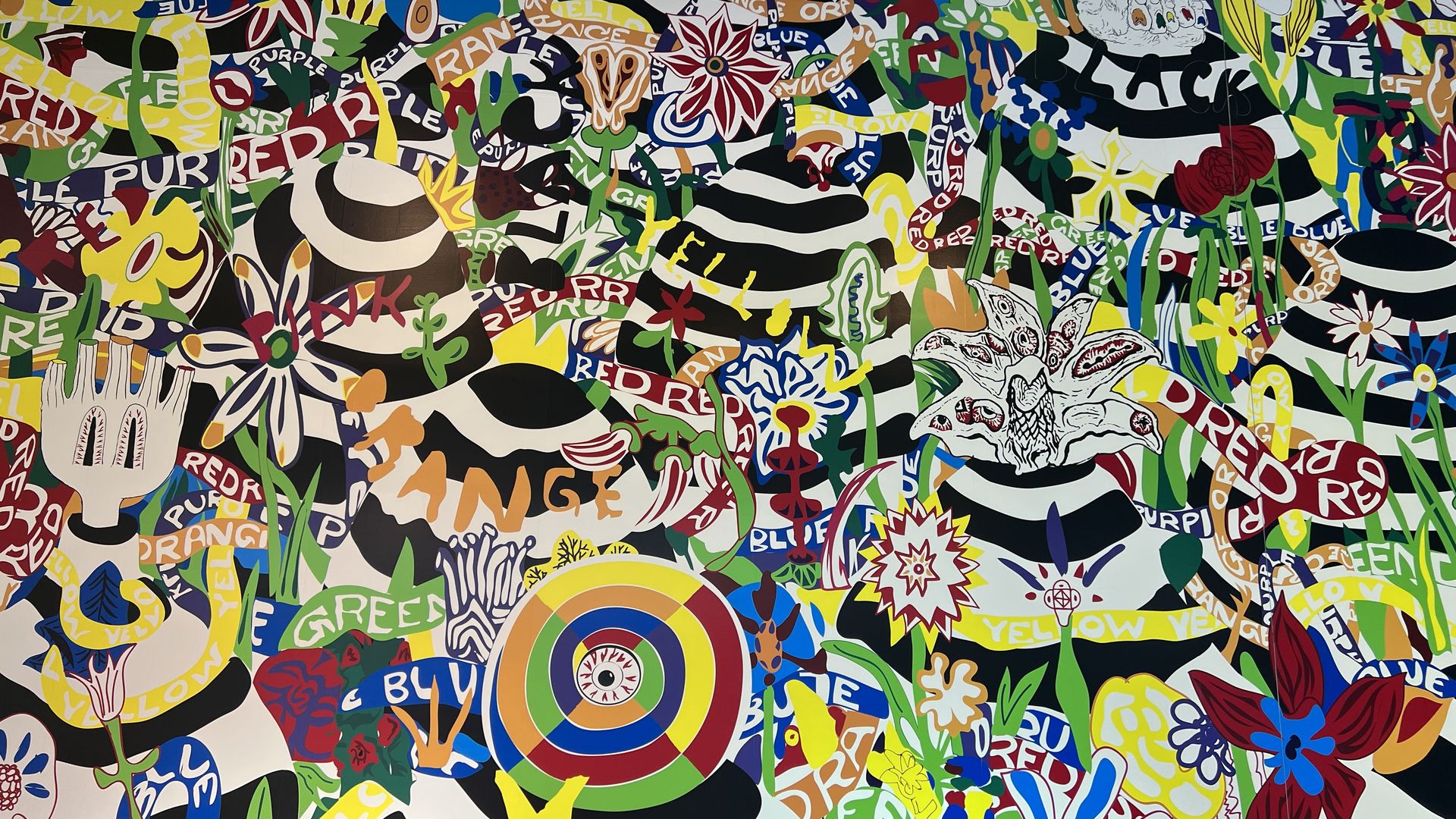 Colorful abstract artwork featuring striped hats, hands, flowers, and scattered words like "RED," "YELLOW," "GREEN," and "BLUE" in vibrant reds, yellows, greens, blues, and purples.