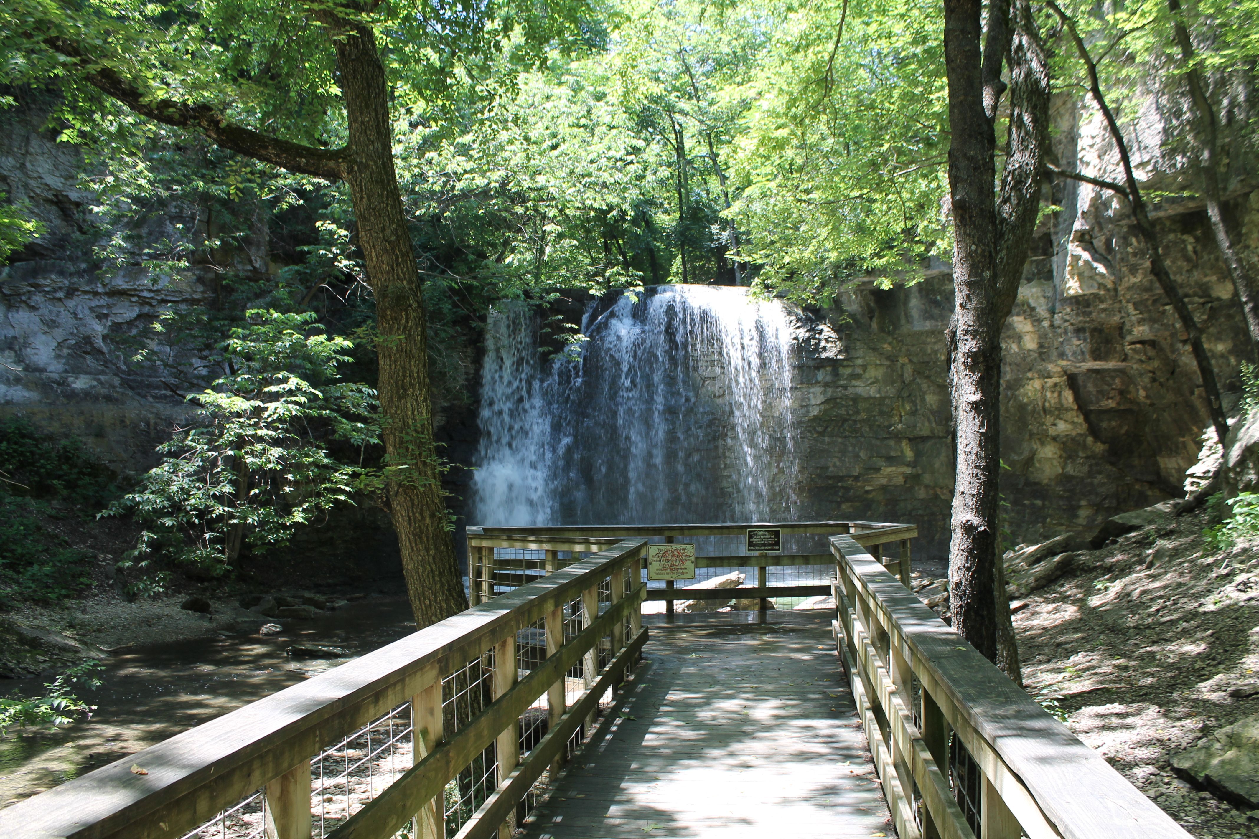 The view of a waterfall at the end of a wooden bridge