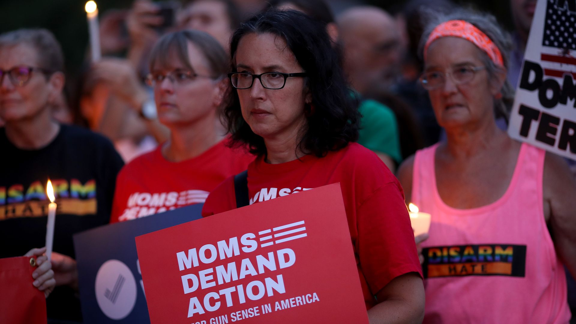 Women holding up pro-gun control signs at a vigil following mass shootings. 