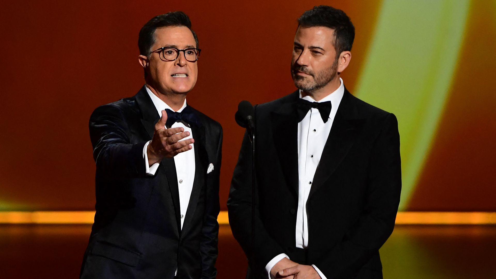 Photo of two men in tuxedos giving a presentation on a stage. 